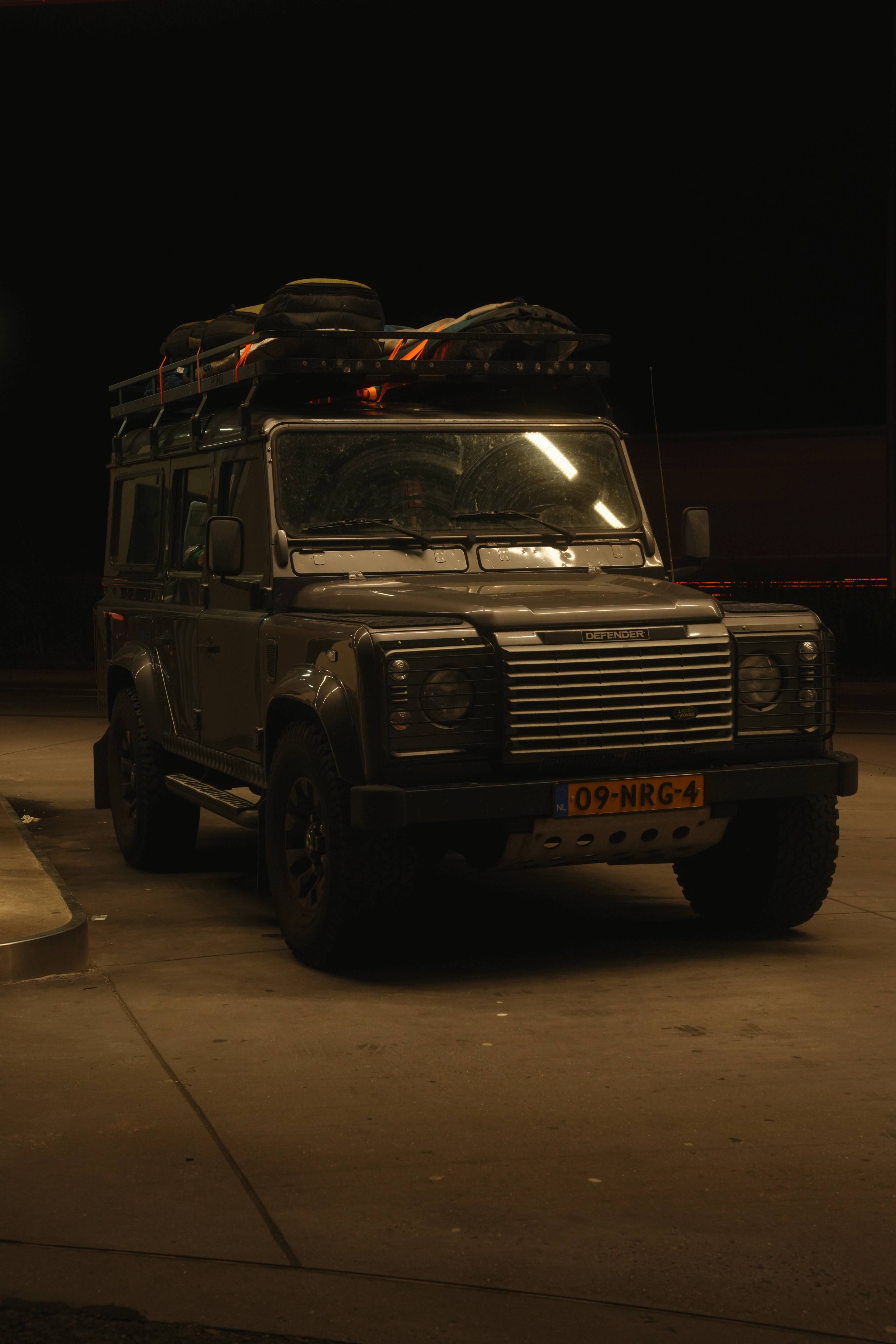 The Landrover under gas-station light at night, gear lashed to the roof, a friend in the driver's seat