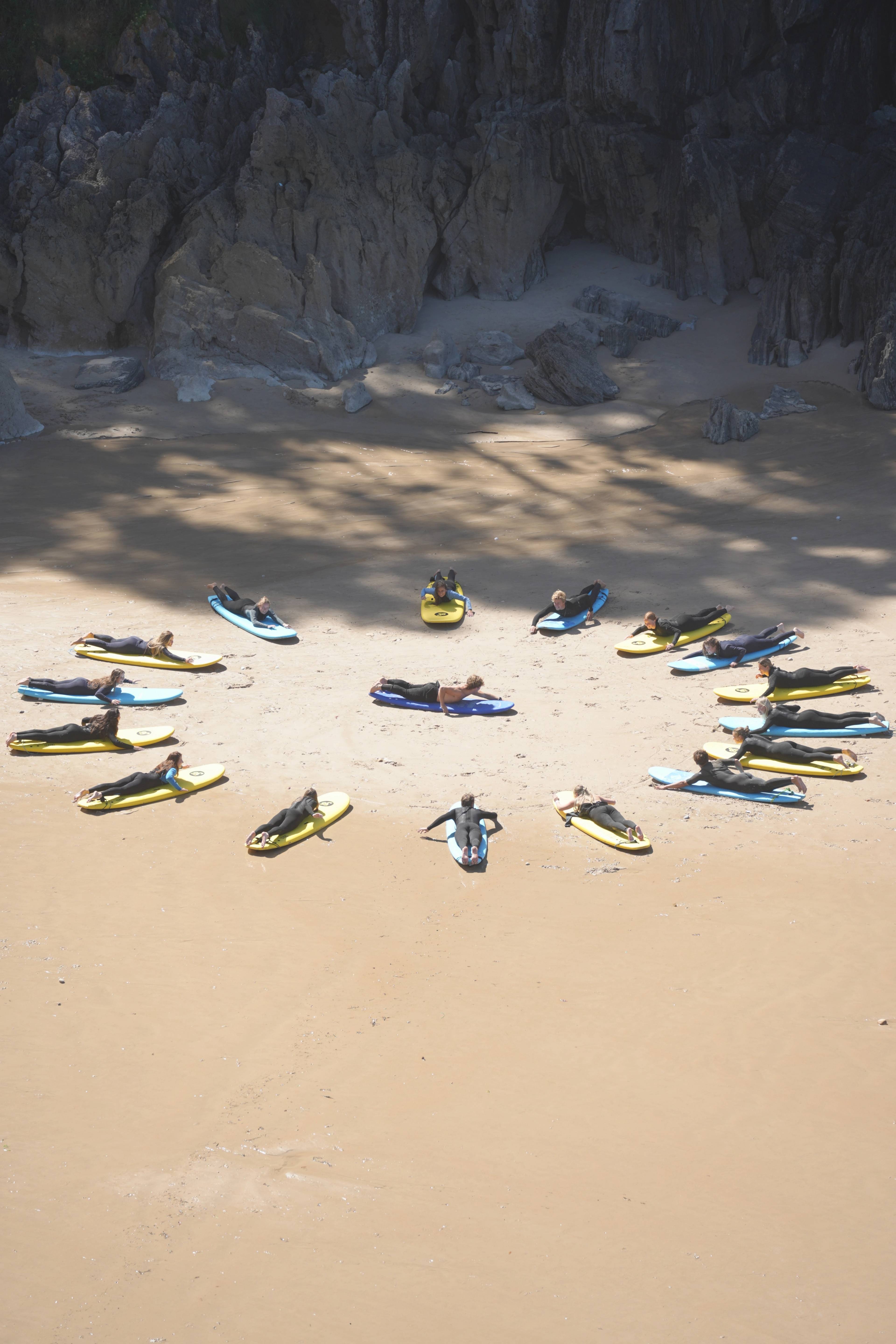 Boards arranged in a heart on the sand, surfers laid out on them