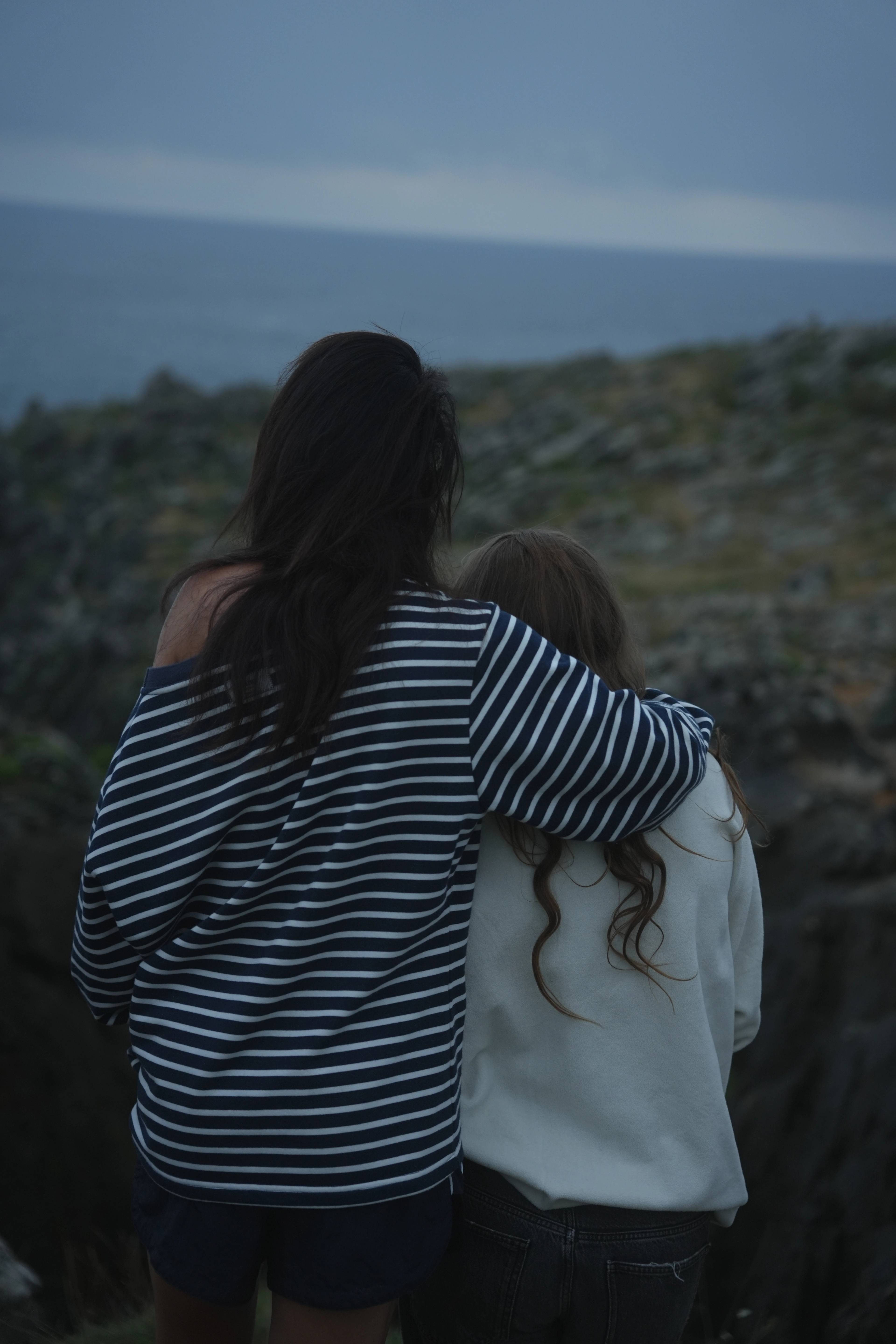 Two arms around each other on the cliff edge, soft blue evening light