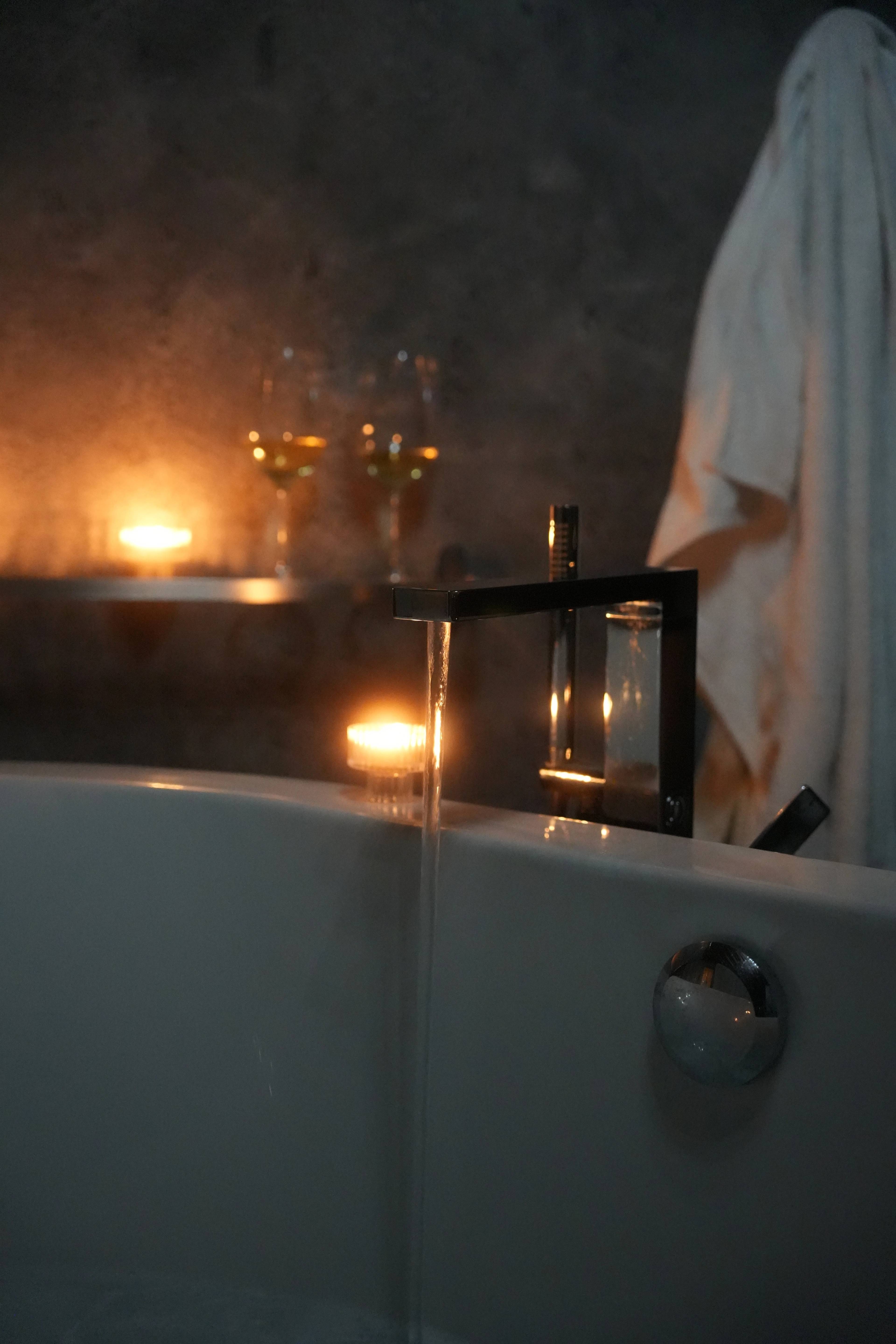Two glasses of white wine and a candle on the tub edge, towel draped over the side