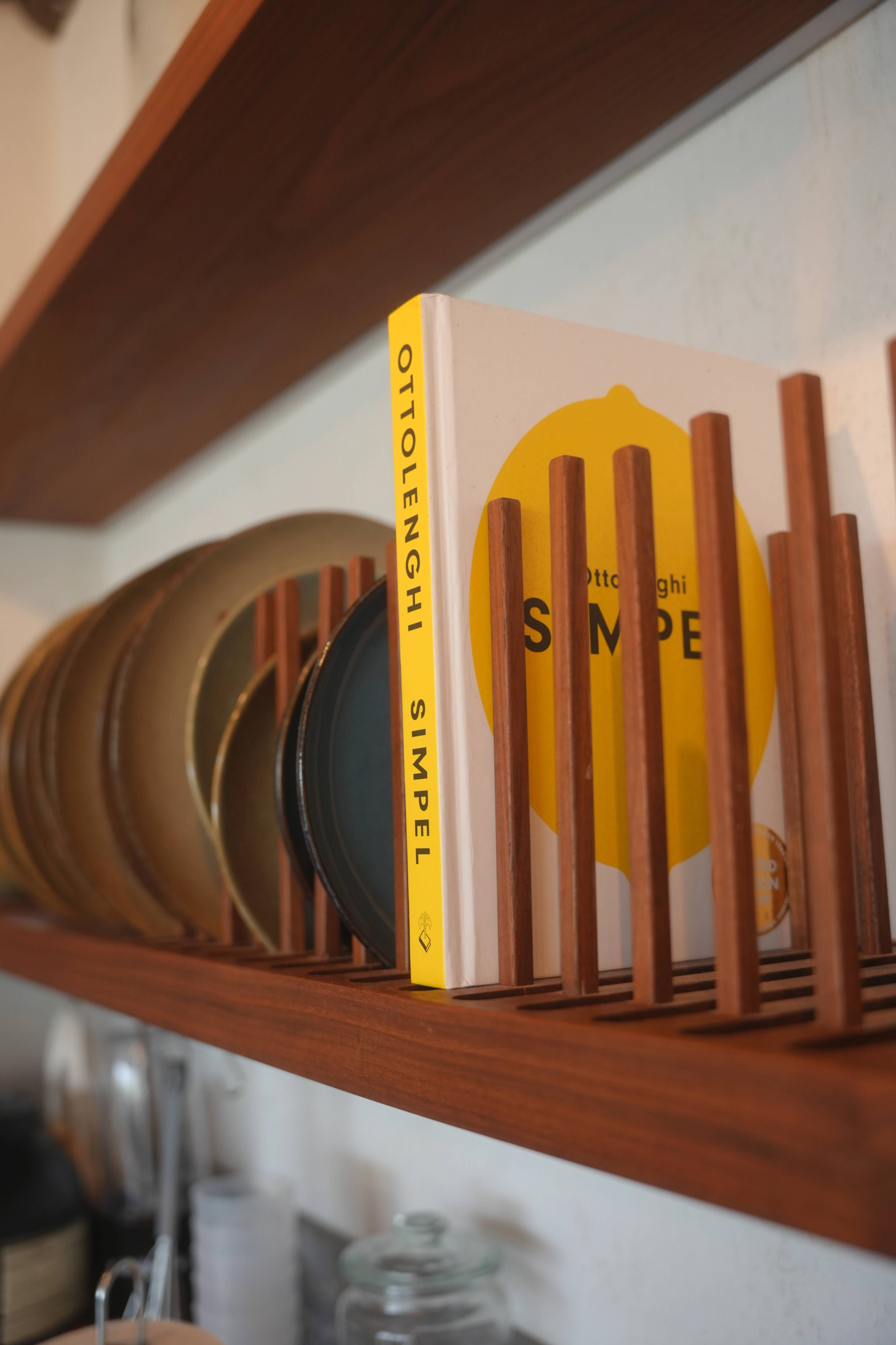Ottolenghi SIMPEL on a wooden plate rack, beside stacked ceramic plates