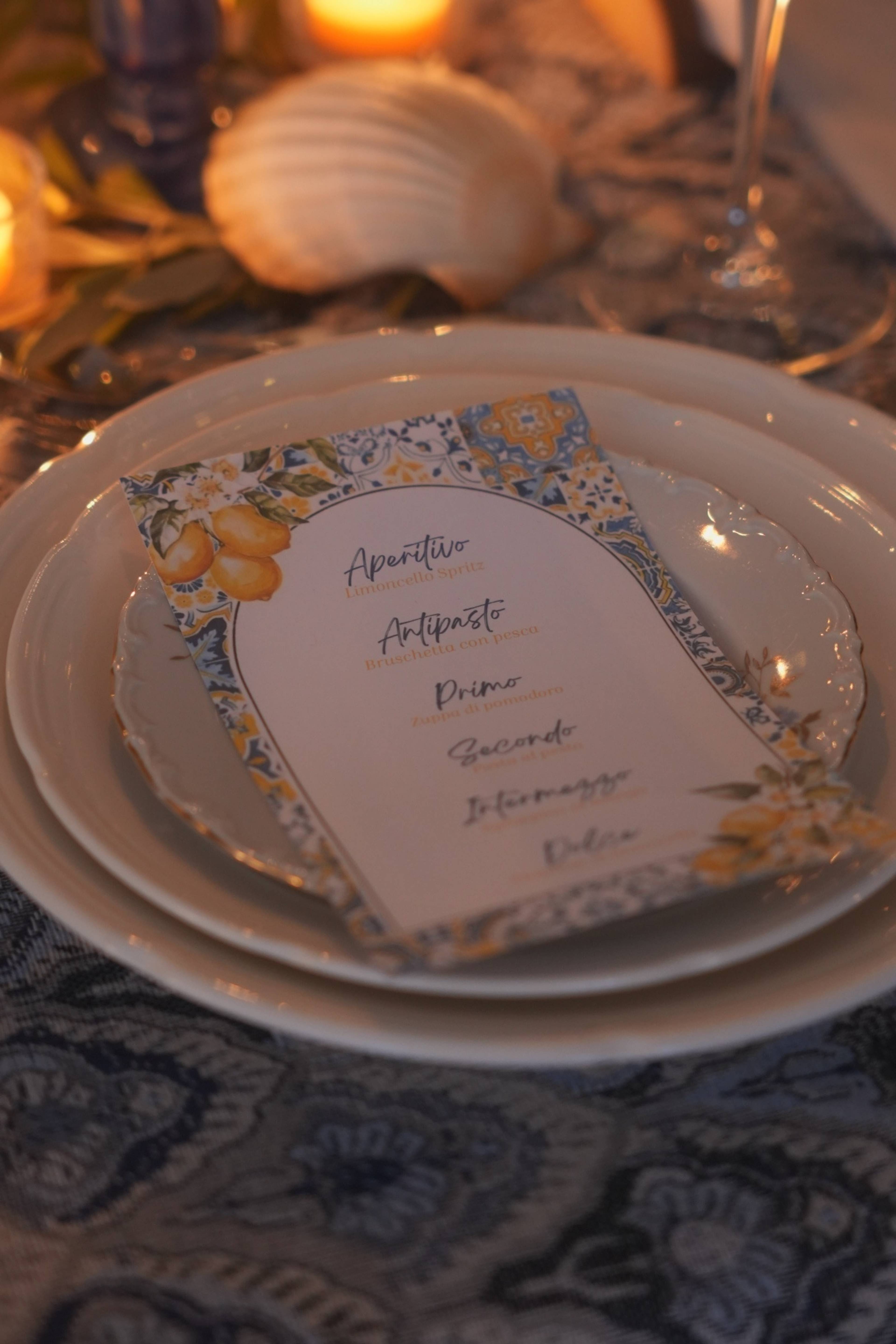 Amalfi-tiled menu card resting on a scalloped plate beside a shell