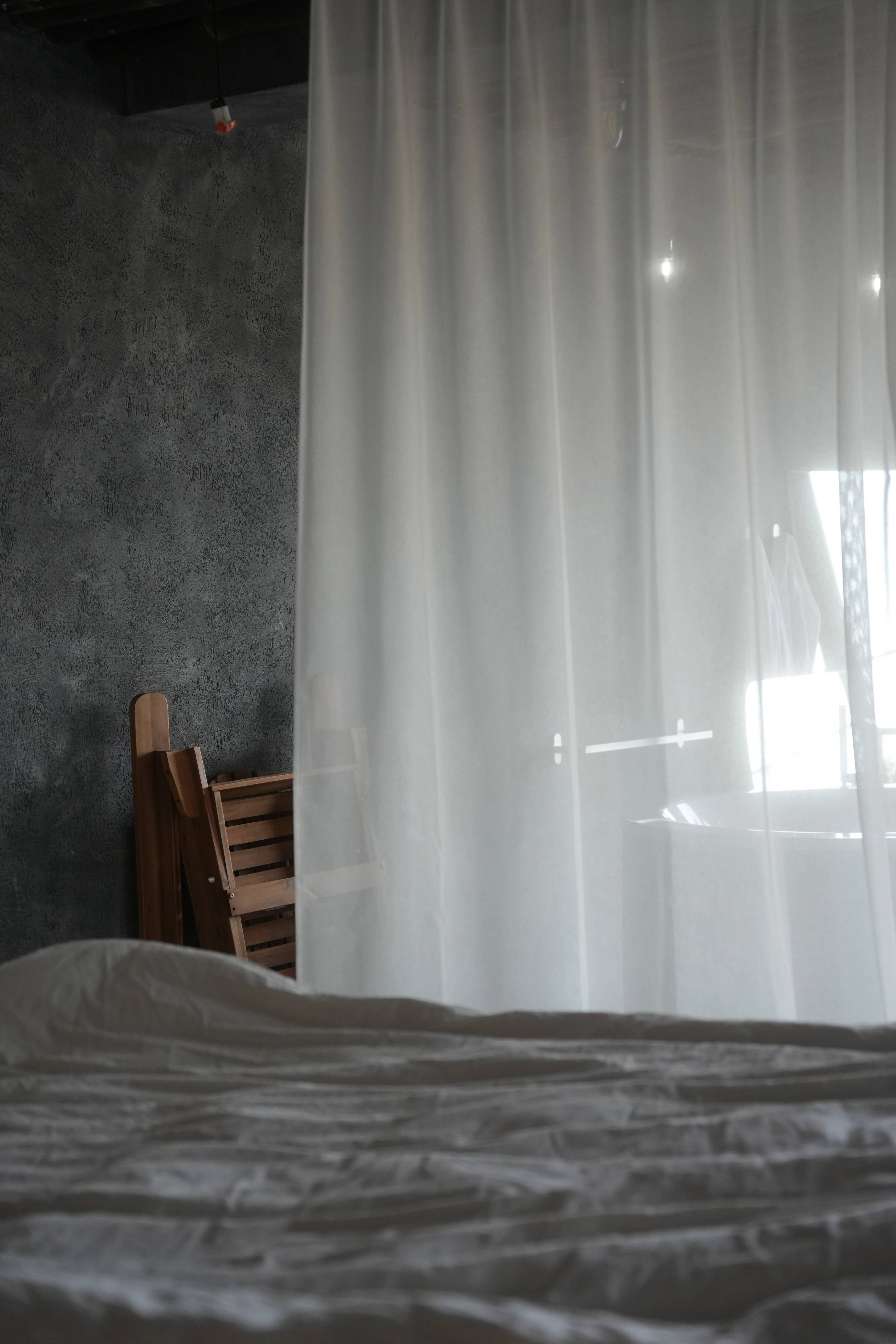 Unmade bed and a sheer curtain glowing in the morning light