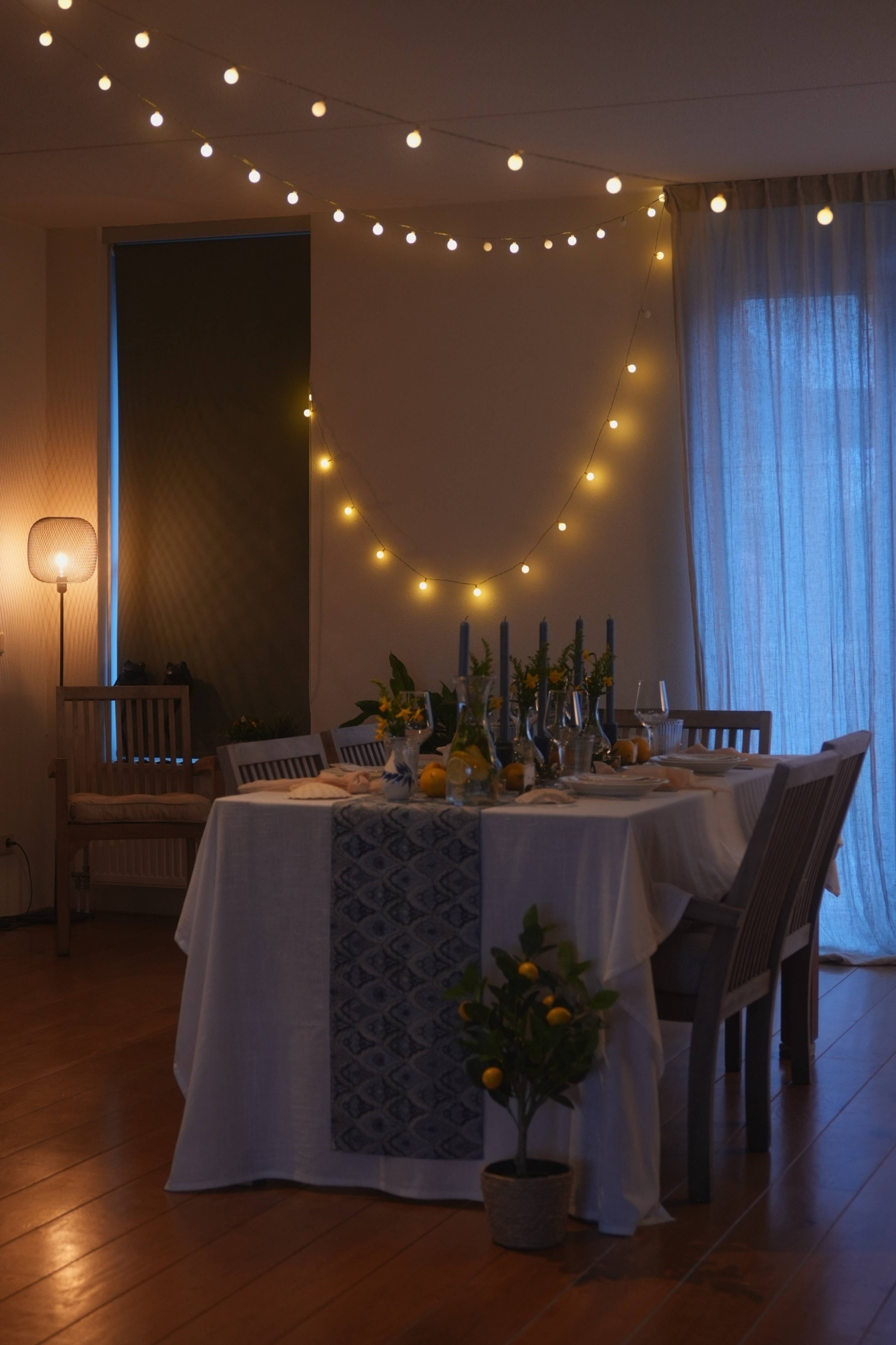 The set table from across the room, string lights overhead and a lemon tree in the foreground