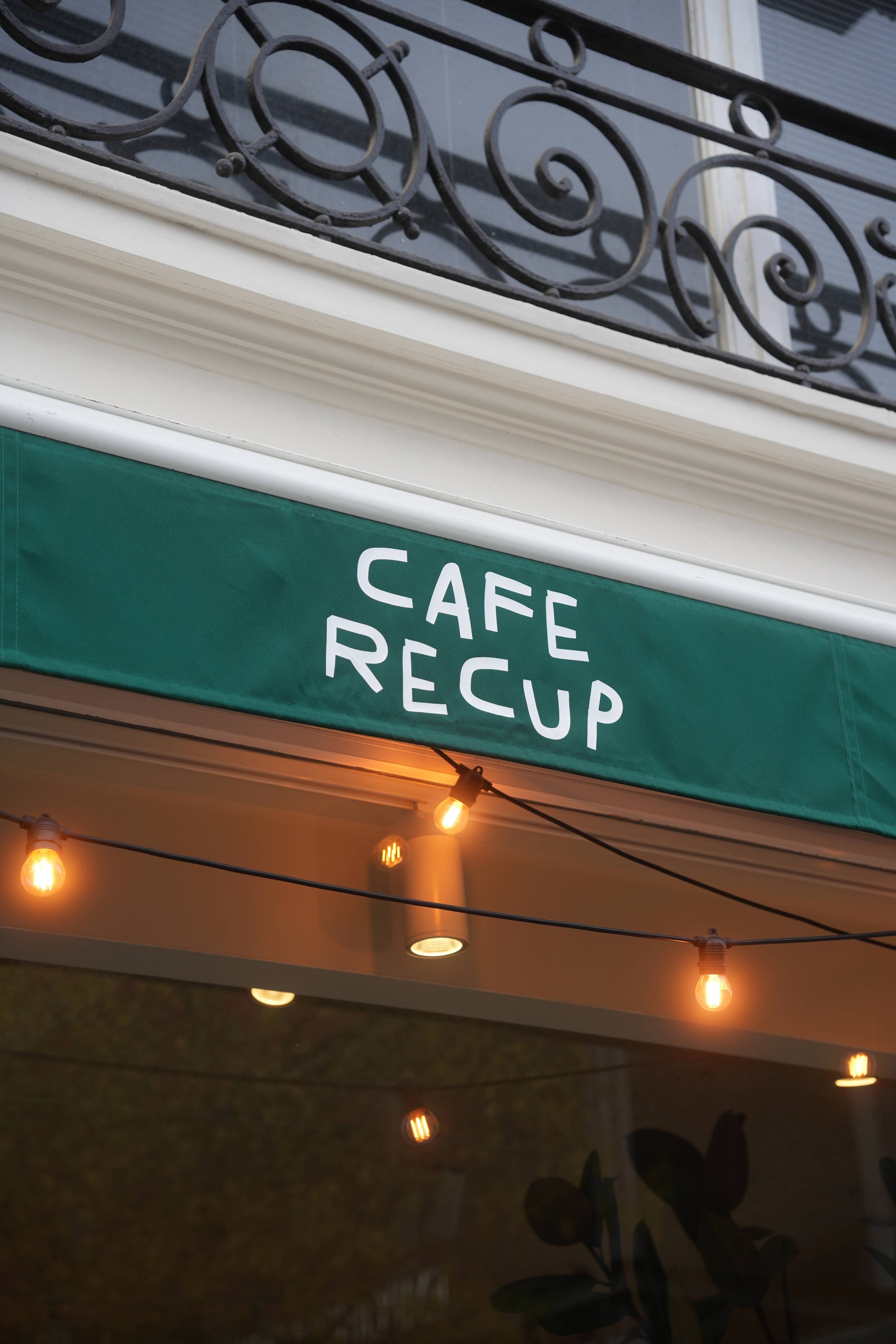The green Café Recup awning seen from beneath, bulbs strung across the entrance