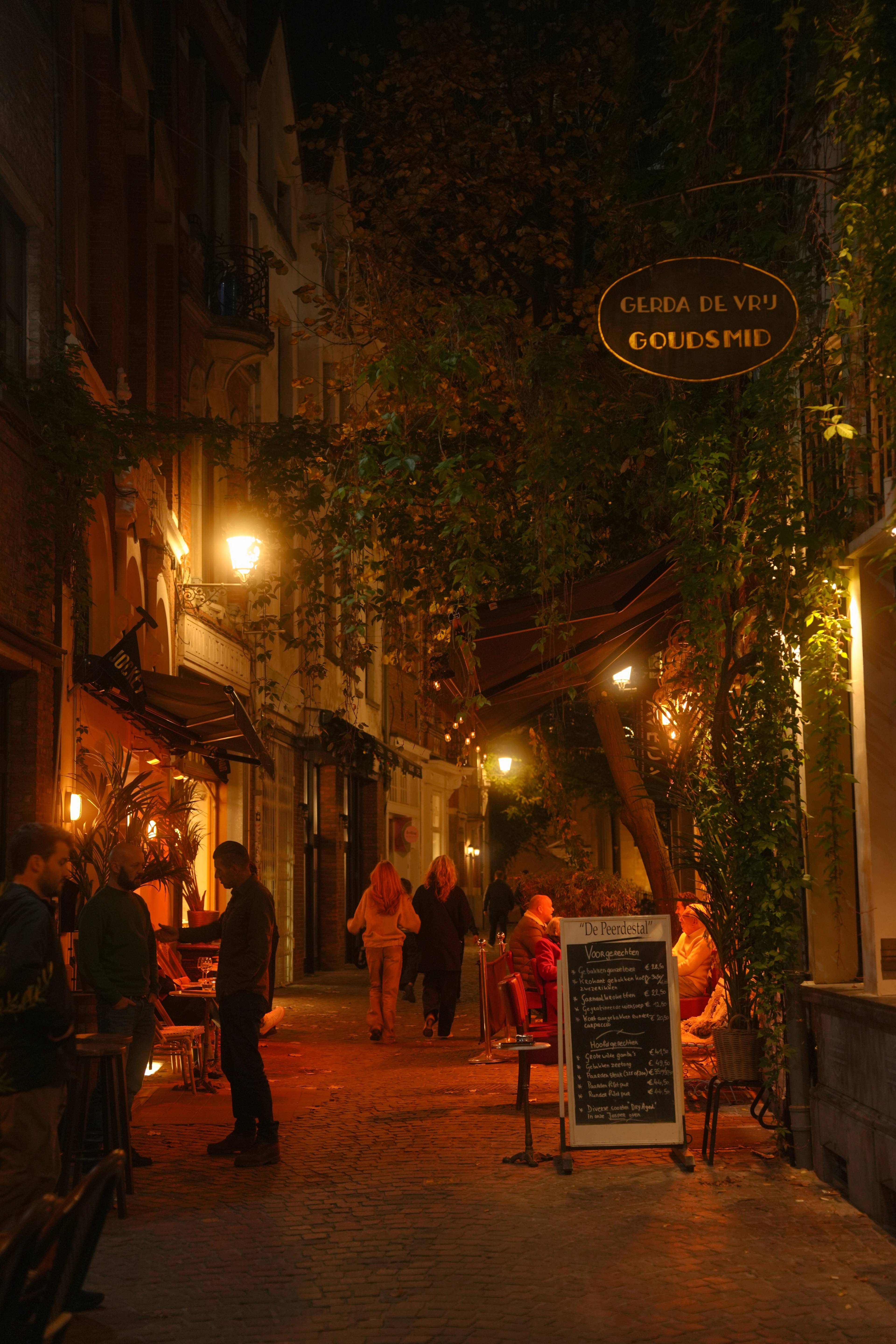 Cobbled lane at night under the Gerda de Vry goldsmith sign, lanterns and a candlelit terrace