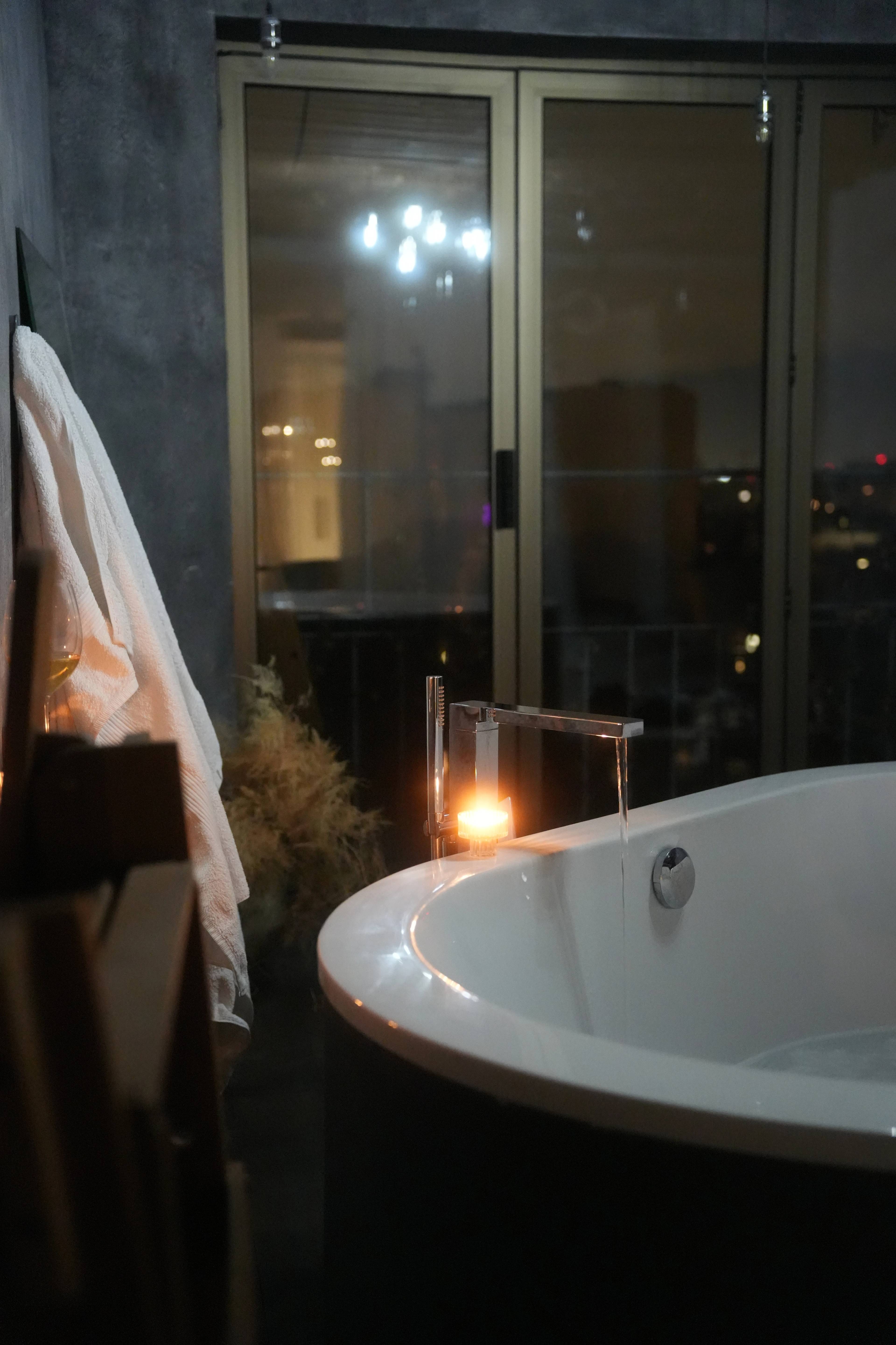 Tub by the window with city lights beyond, pampas grass in the corner