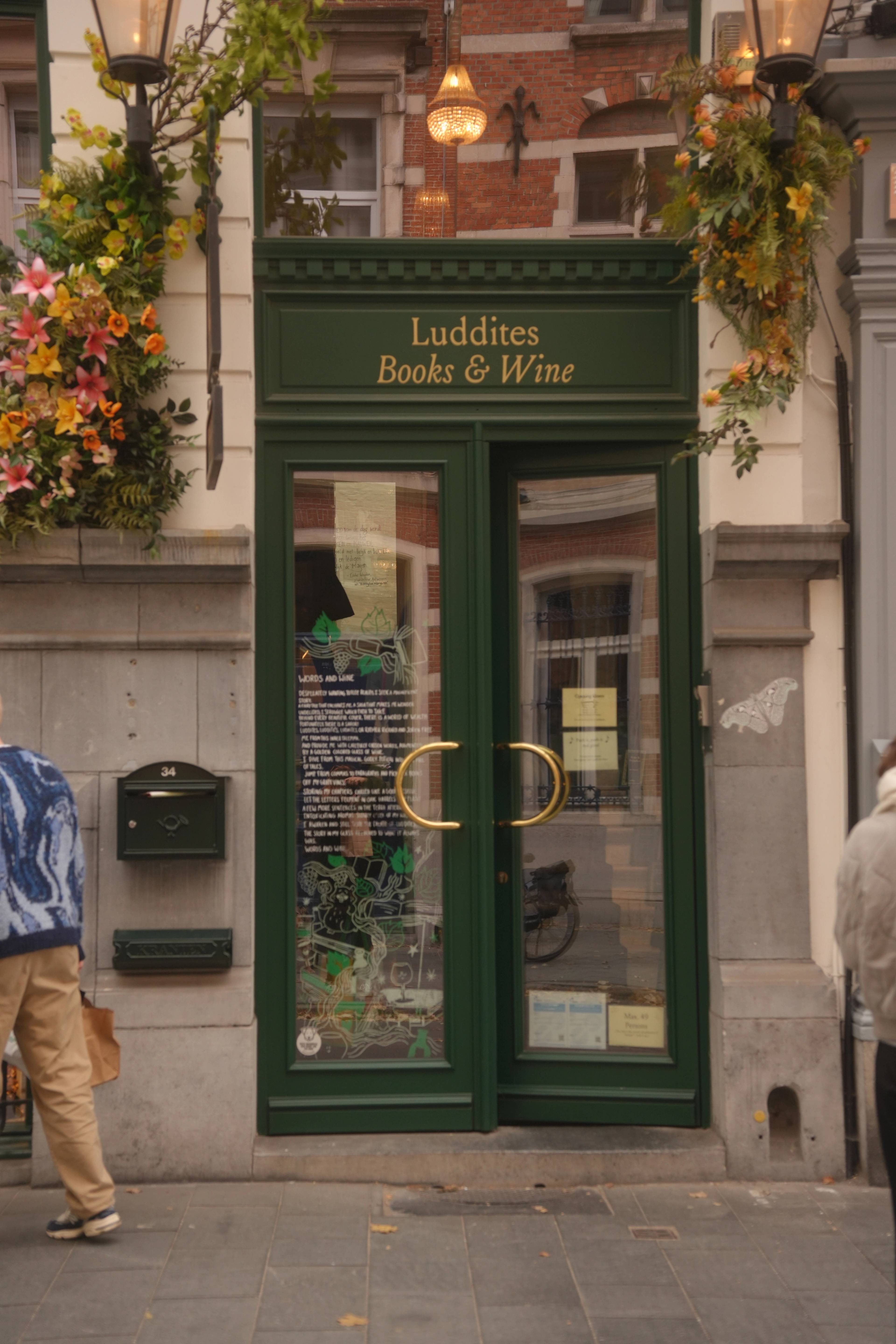 Green storefront of Luddites Books & Wine, flowers spilling from the brackets above