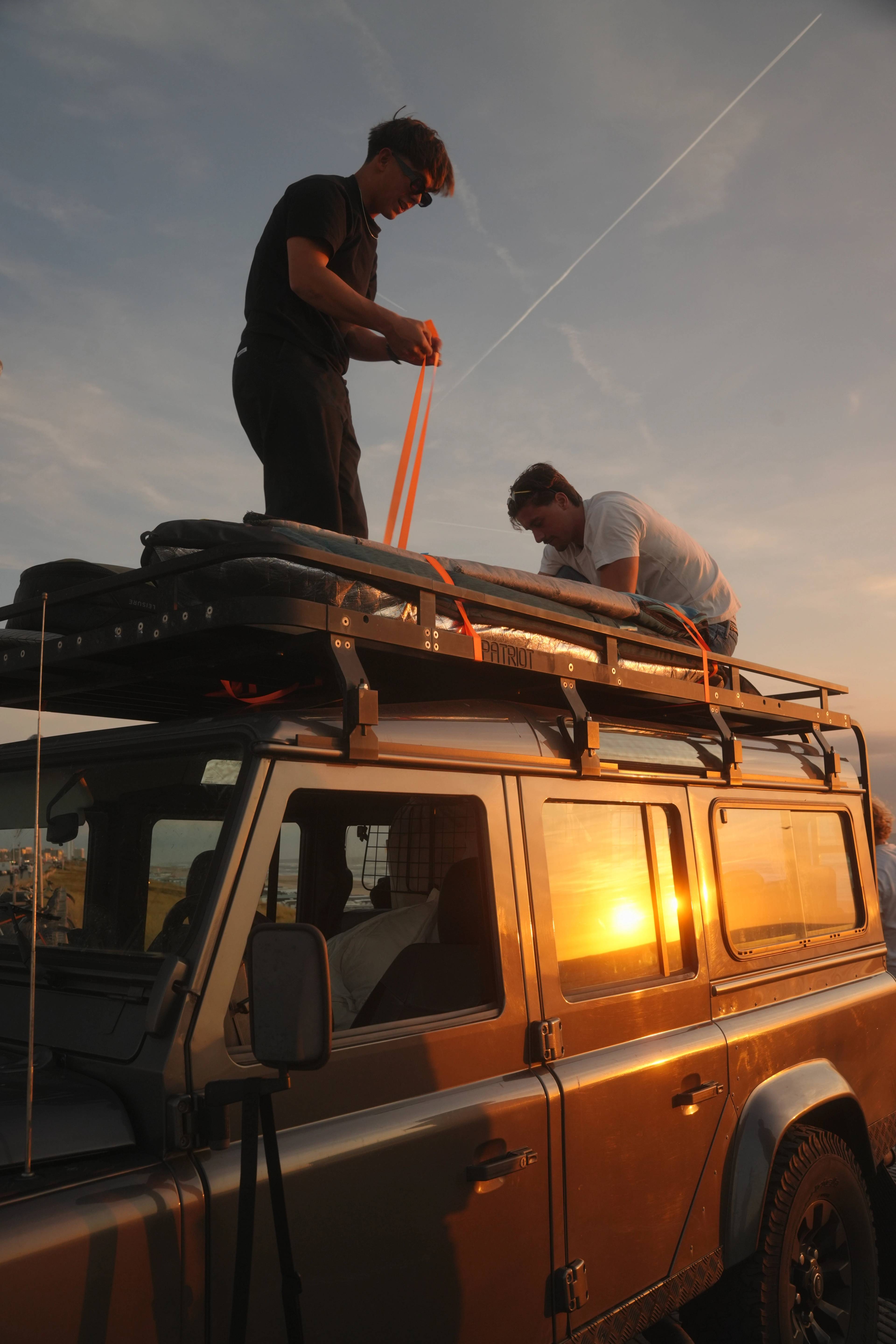 Two friends up on the Landrover roof at sunset, strapping down the gear