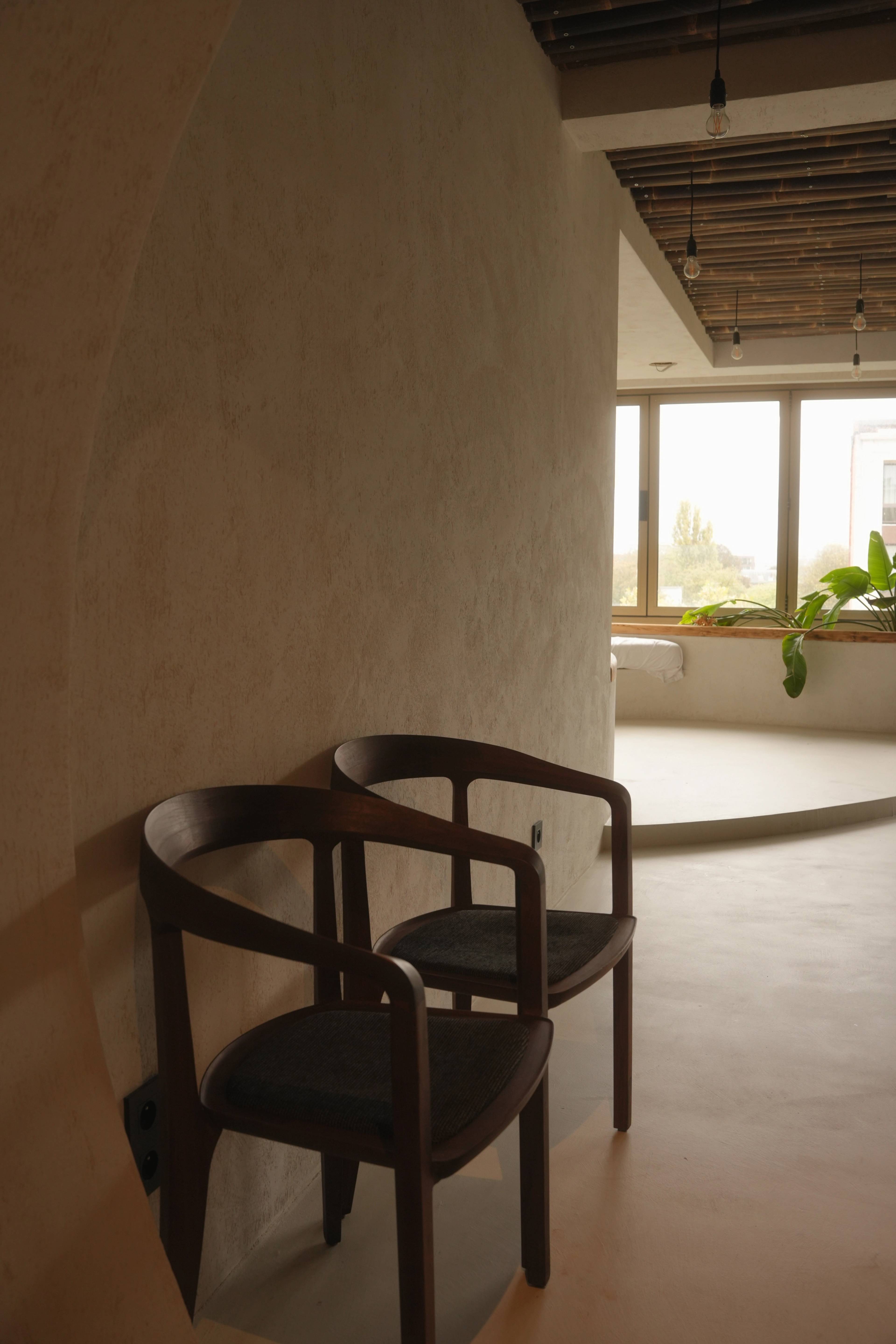 Two dark wood chairs against a curved plaster wall, soft daylight from the corner window