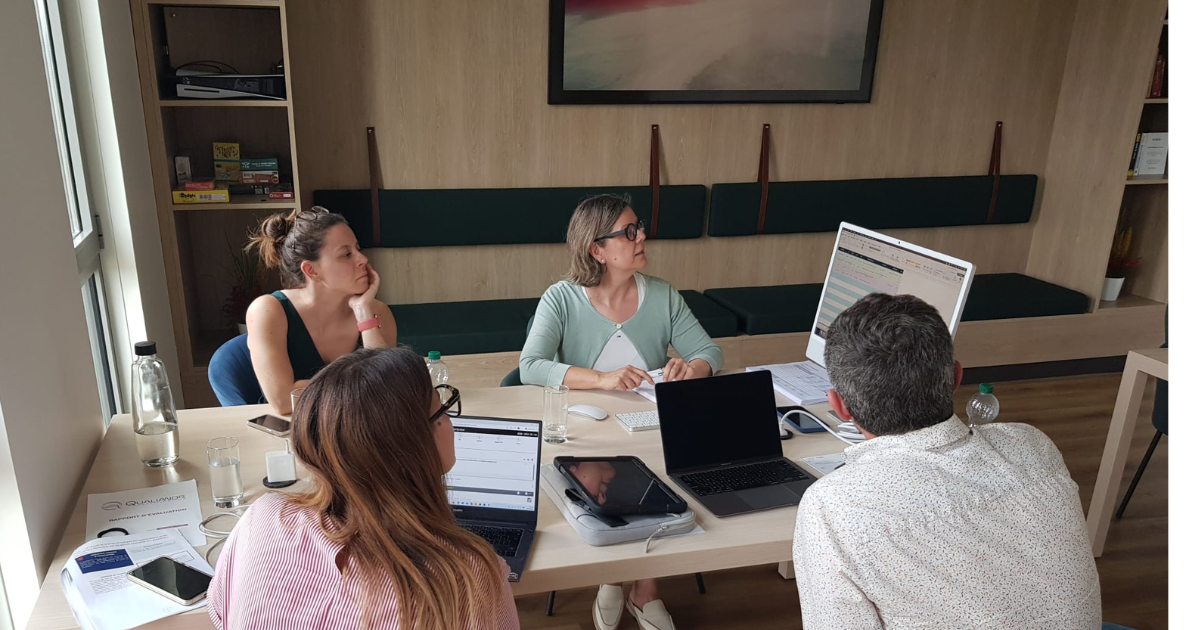 Groupe de 4 personnes (3 femmes et un homme) assis autour d'une table regardant un écran d'ordinateur et présentant des documents pour la certification Qualiopi.