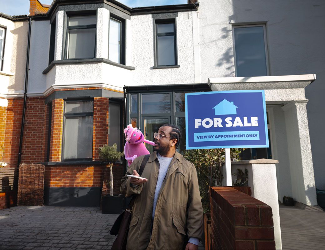 A person standing outside a house with a “For Sale” sign