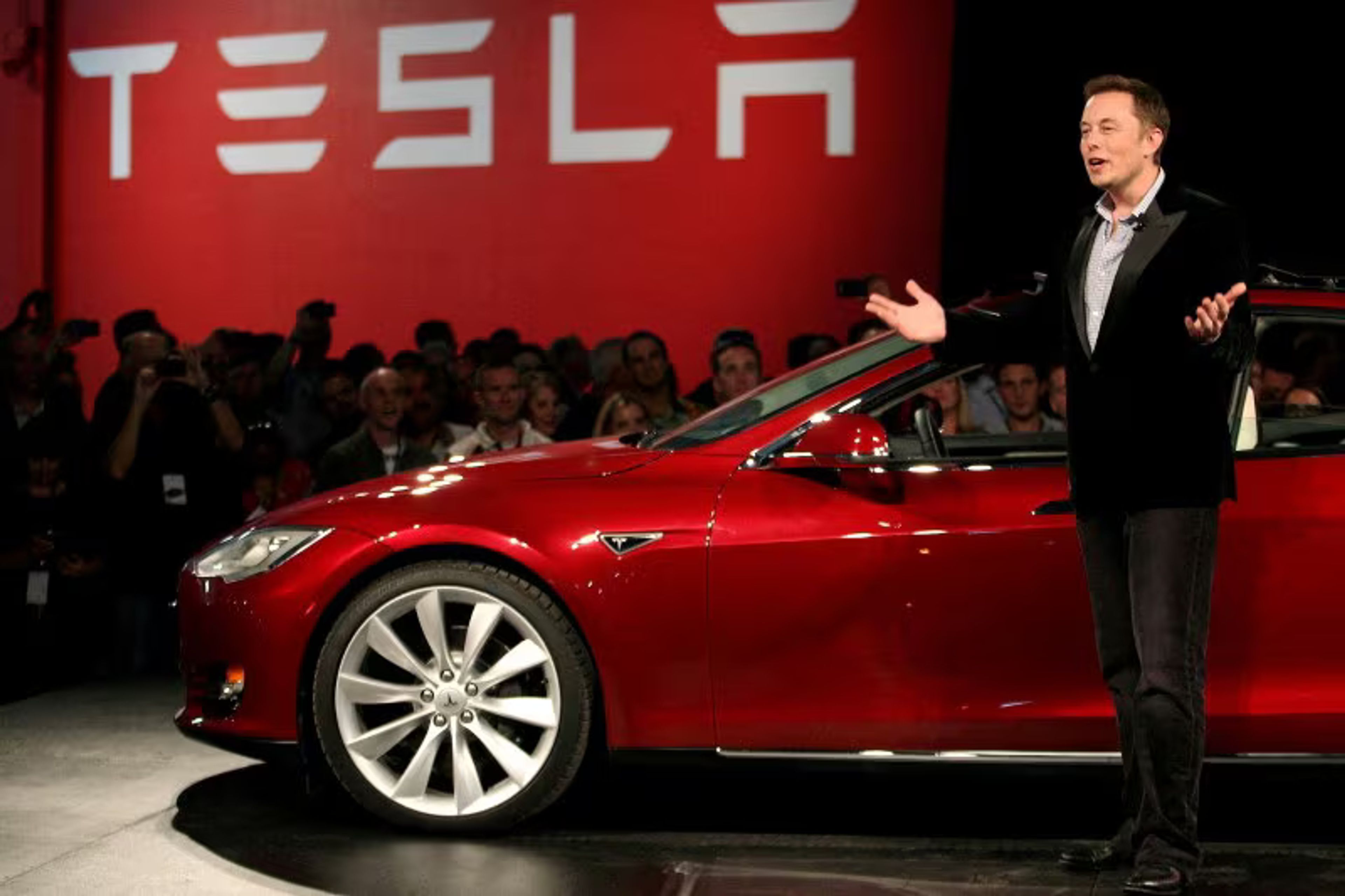 Tesla logo with a boardroom table and hospitality concept graphics in the background, symbolizing corporate expansion