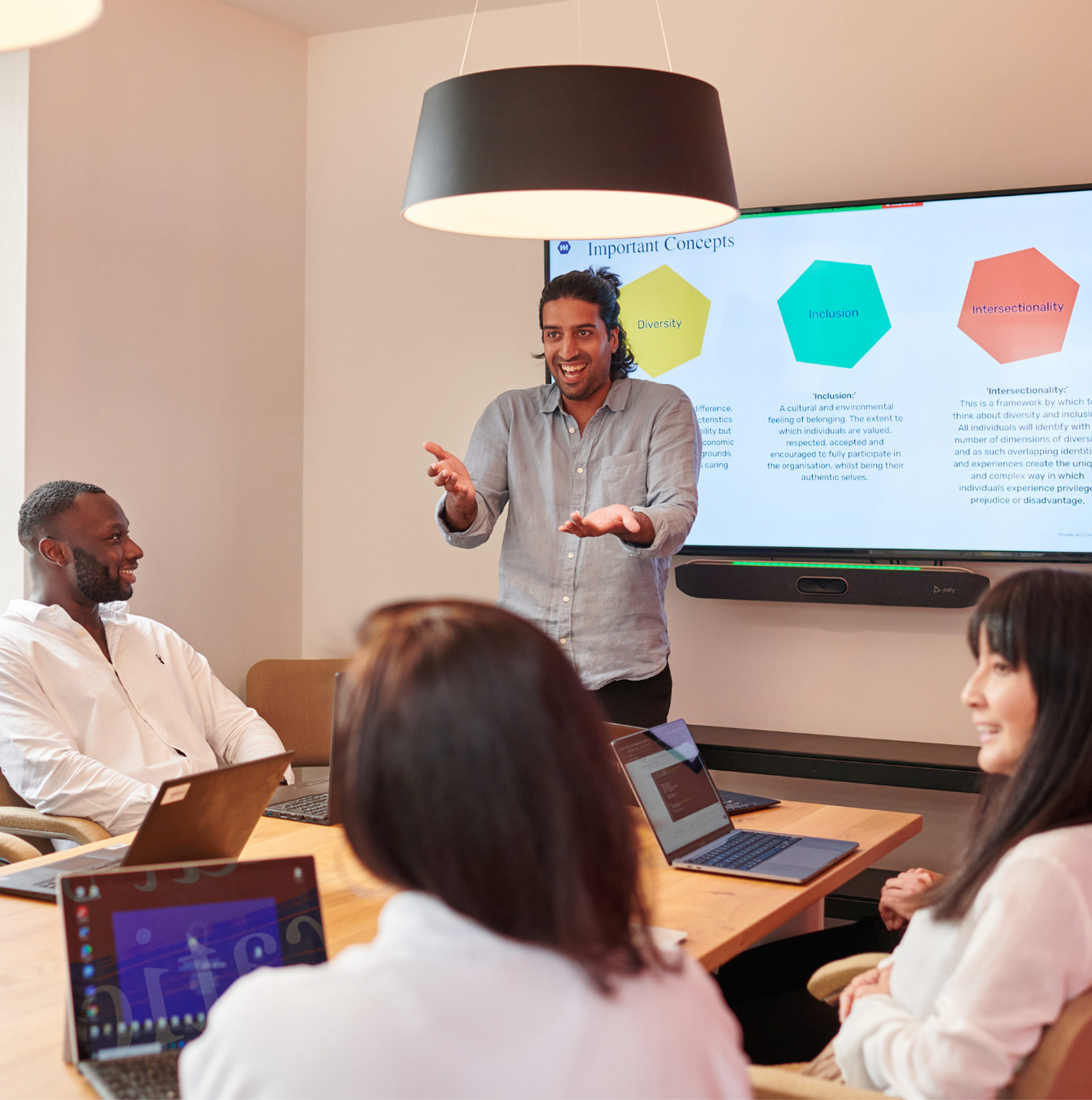 A man in a light blue shirt presenting in a meeting room with 3 individuals