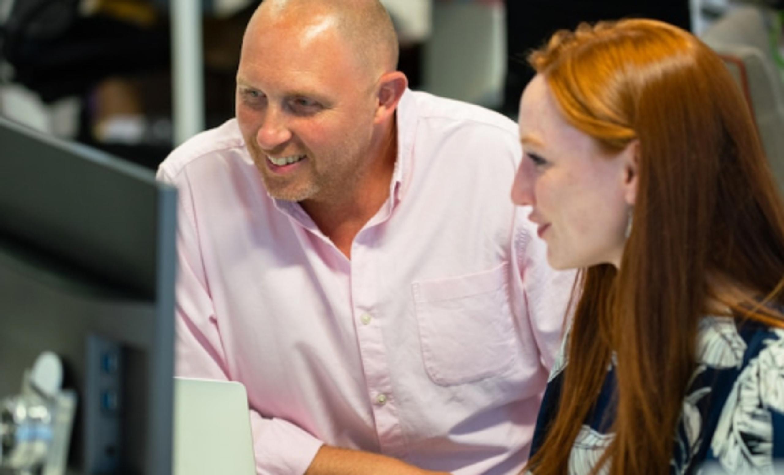 Two people smiling, working on a computer together