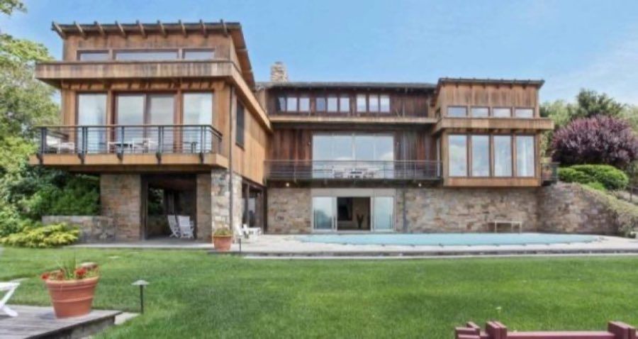 Rear elevation of a mid-century modern house in cedar and fieldstone, with deep balconies, banked windows and a lap pool along the lawn.