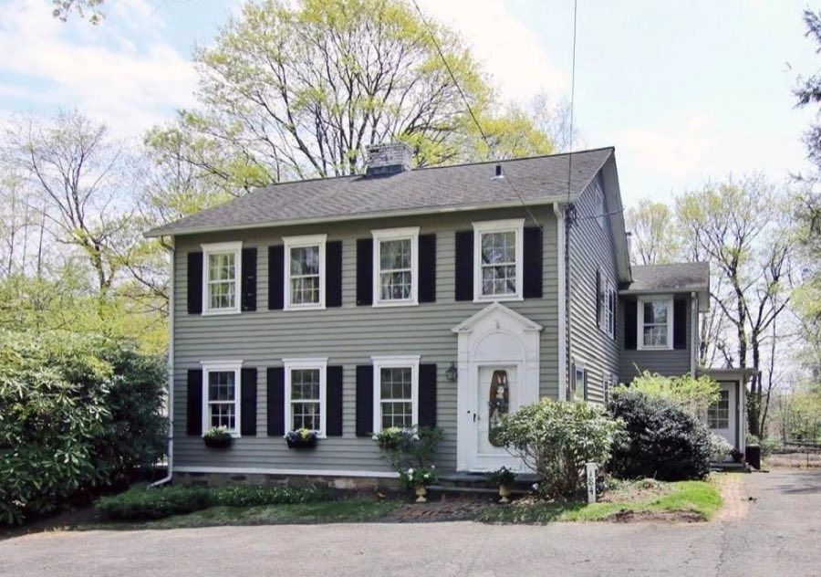 Sage green clapboard colonial with black shutters, white trim and a scrolled pediment over the front door, beside a gravel turnaround.