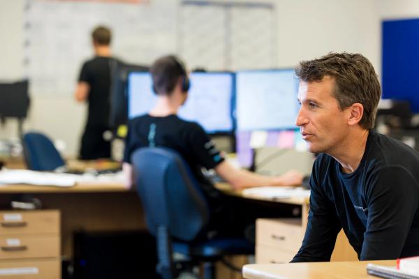 Aerial view of a serene tropical island with lush greenery surrounded by turquoise sea. Boats dot the water near the sandy shore, under a clear sky.