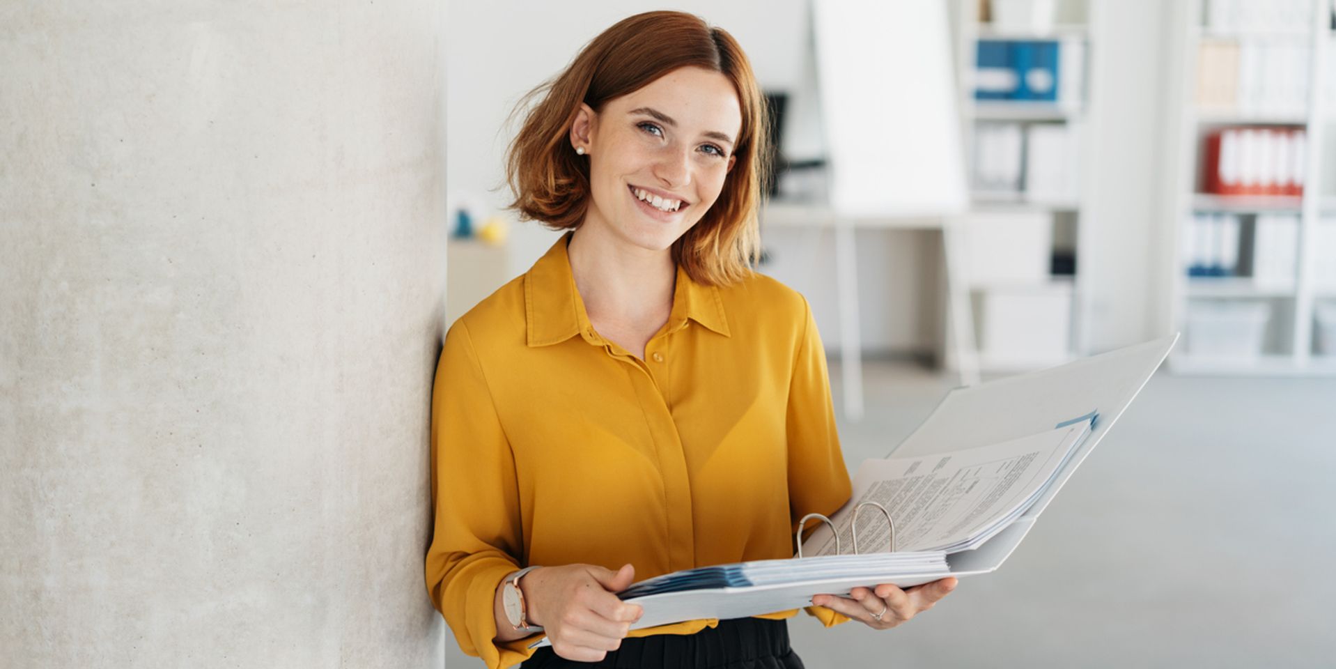 Attractive young office worker holding a large open binder as she looks at the camera with a sweet friendly smile
