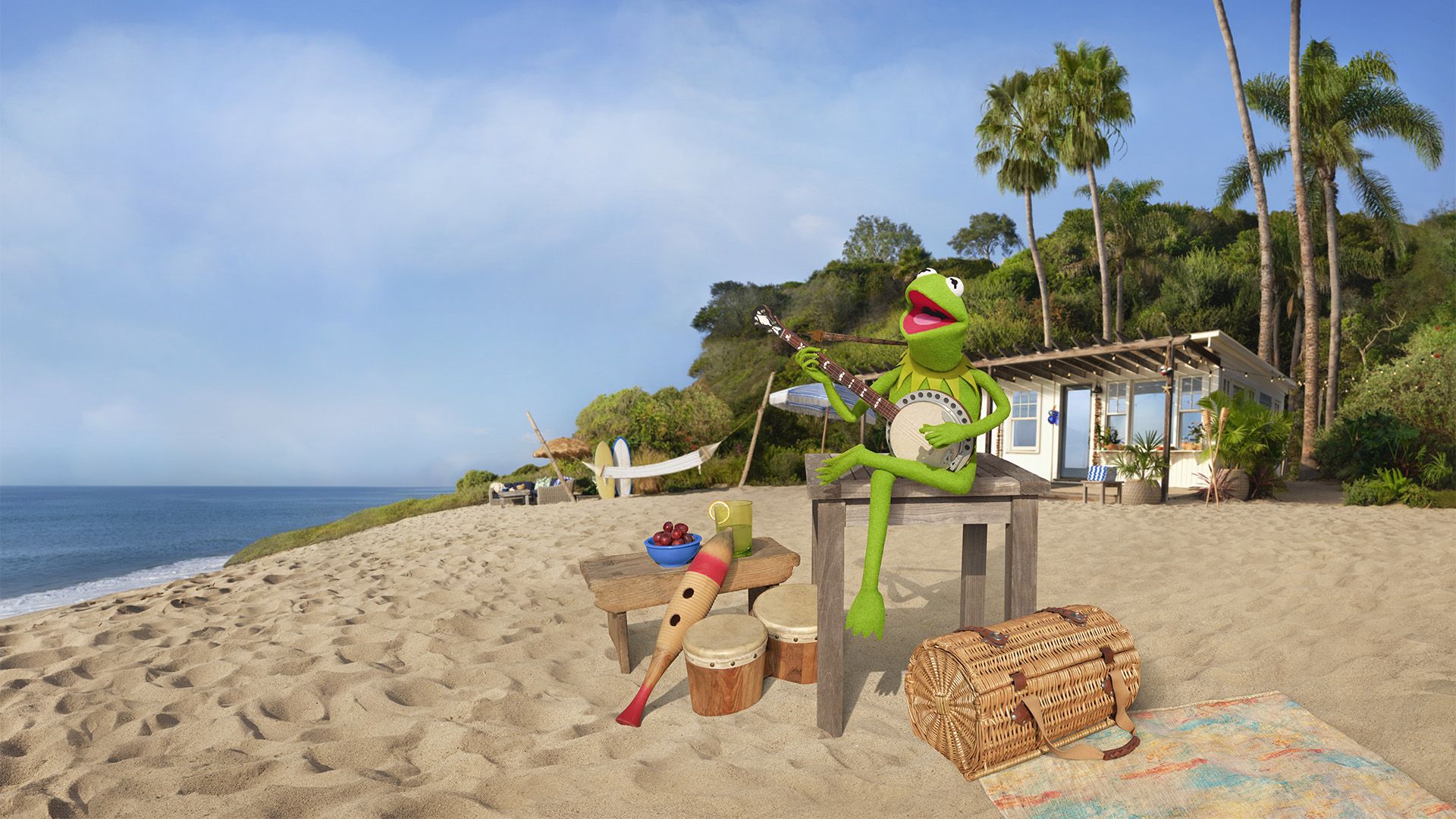 A photo of Kermit the frog playing a banjo on a beach in front of his rented beach house