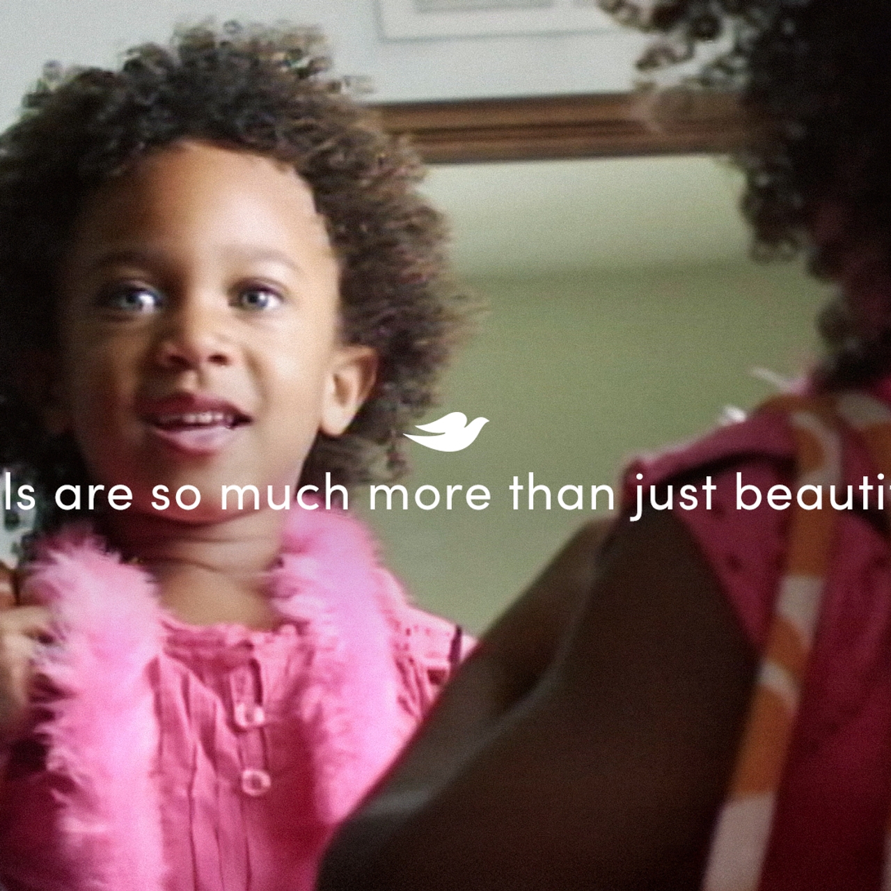 Still from video. Girl looking in a mirror. Text overlay says Girls are so much more than just beautiful.