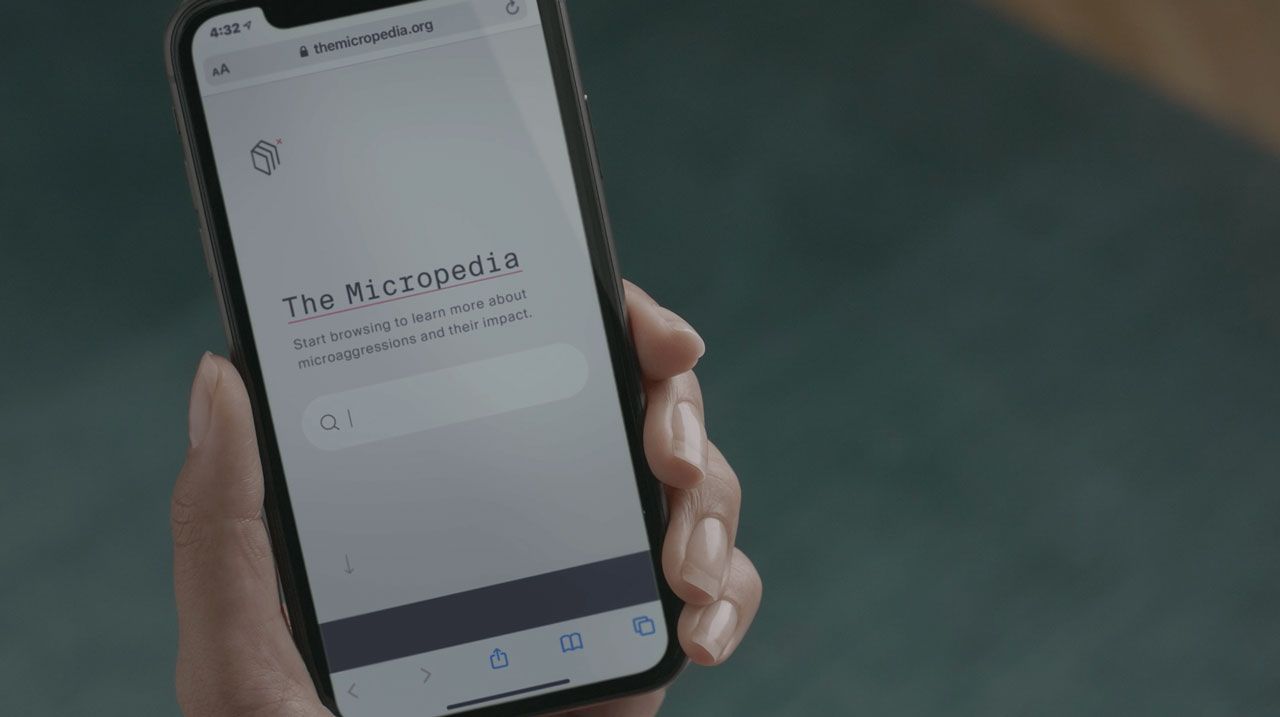 A hand holding a phone displaying the Micropedia of Microaggression website. 