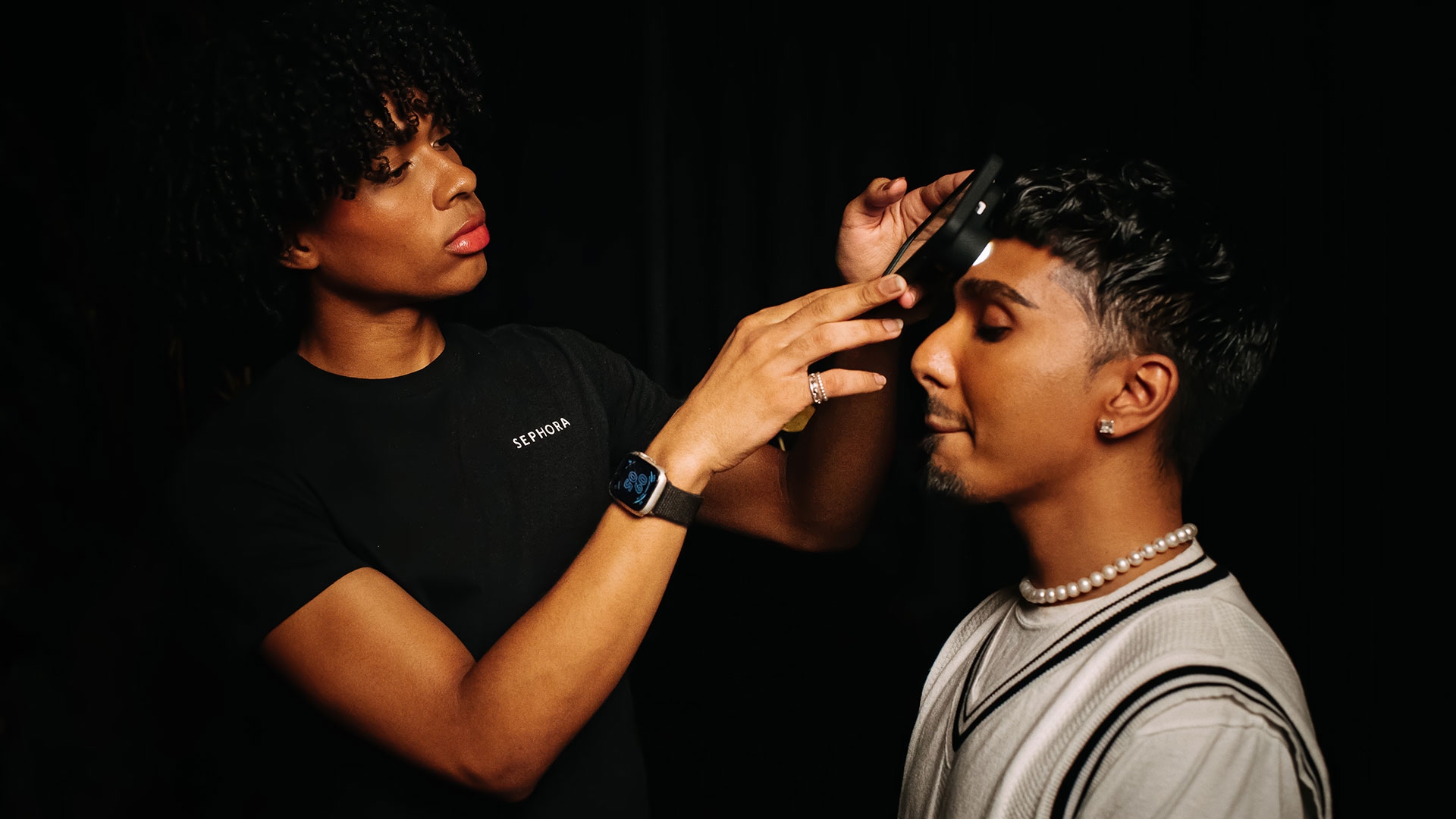 A women using a smartphone to scan the skin tones of a mans face.