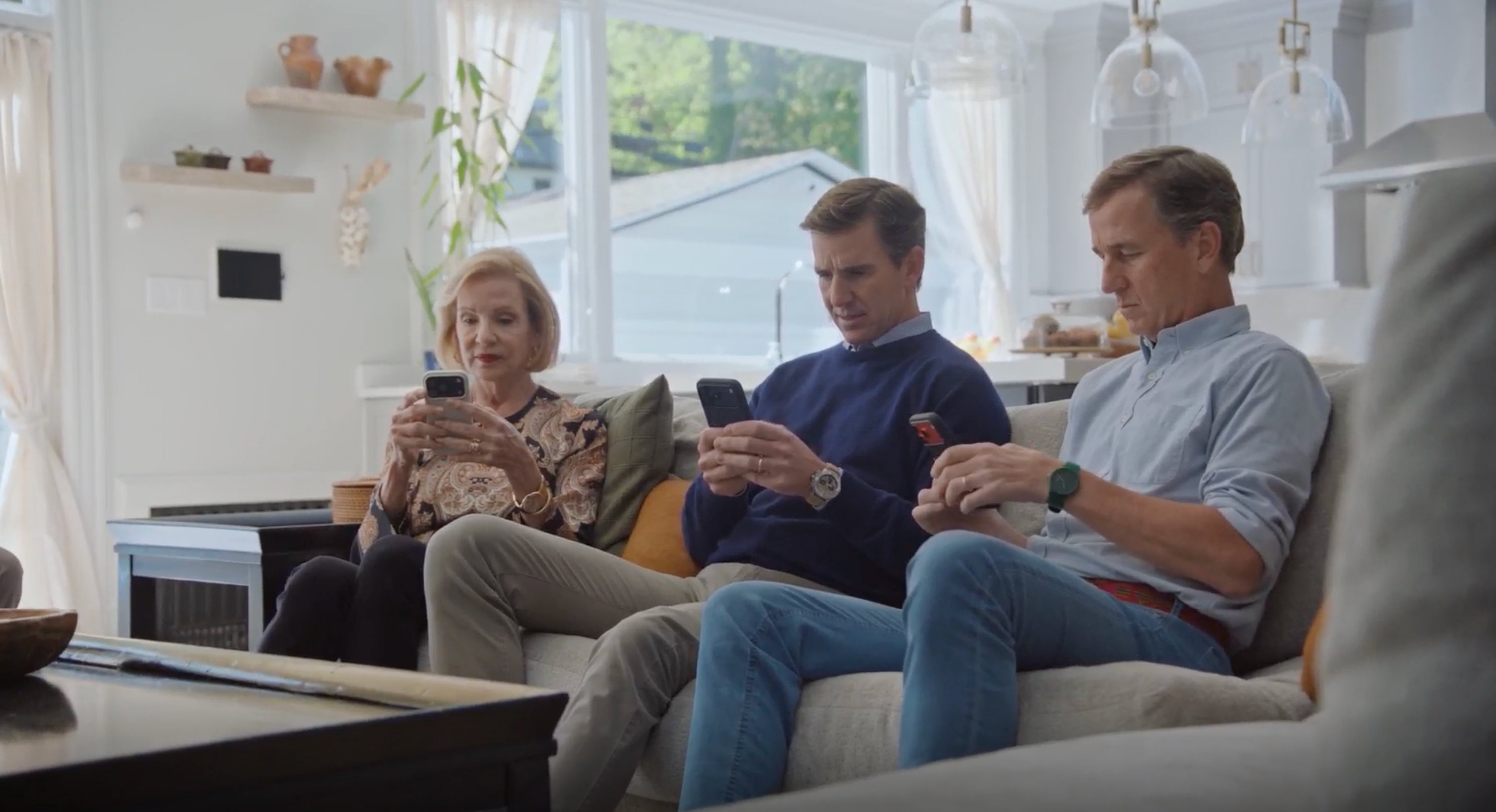 Three people sit on a couch in a bright living room, each focused on their smartphones.