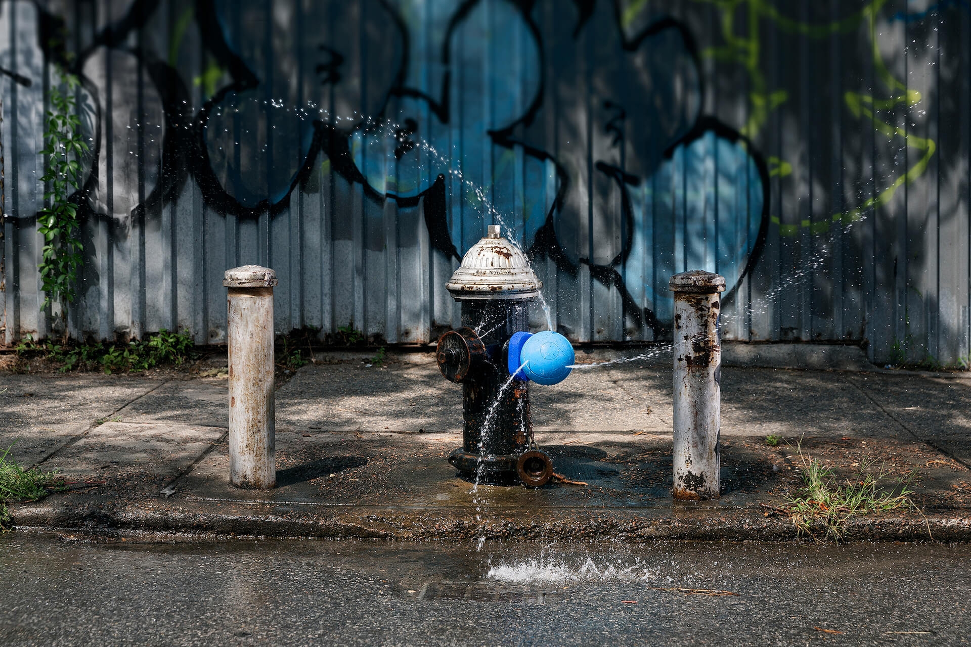An old New York City fire hydrant with a blue Splash Spot fire hydrant cap sprinkling water in three directions.