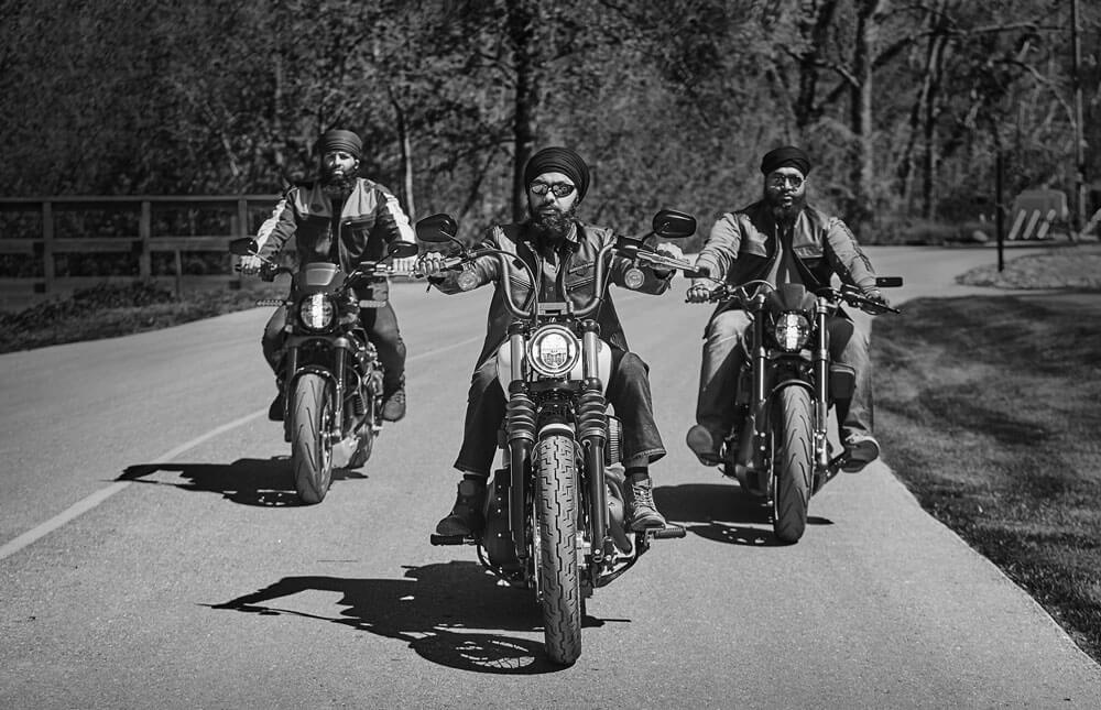 Three men wearing turbans riding Harley Davidson motorcycles, cruising confidently down the road.