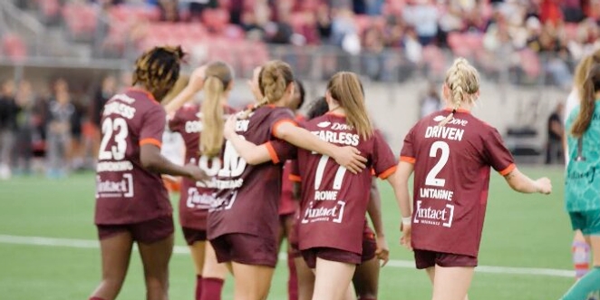 A group of female soccer players in maroon jerseys with motivational words like "FEARLESS" and "DRIVEN" walk off the field together, showing camaraderie.