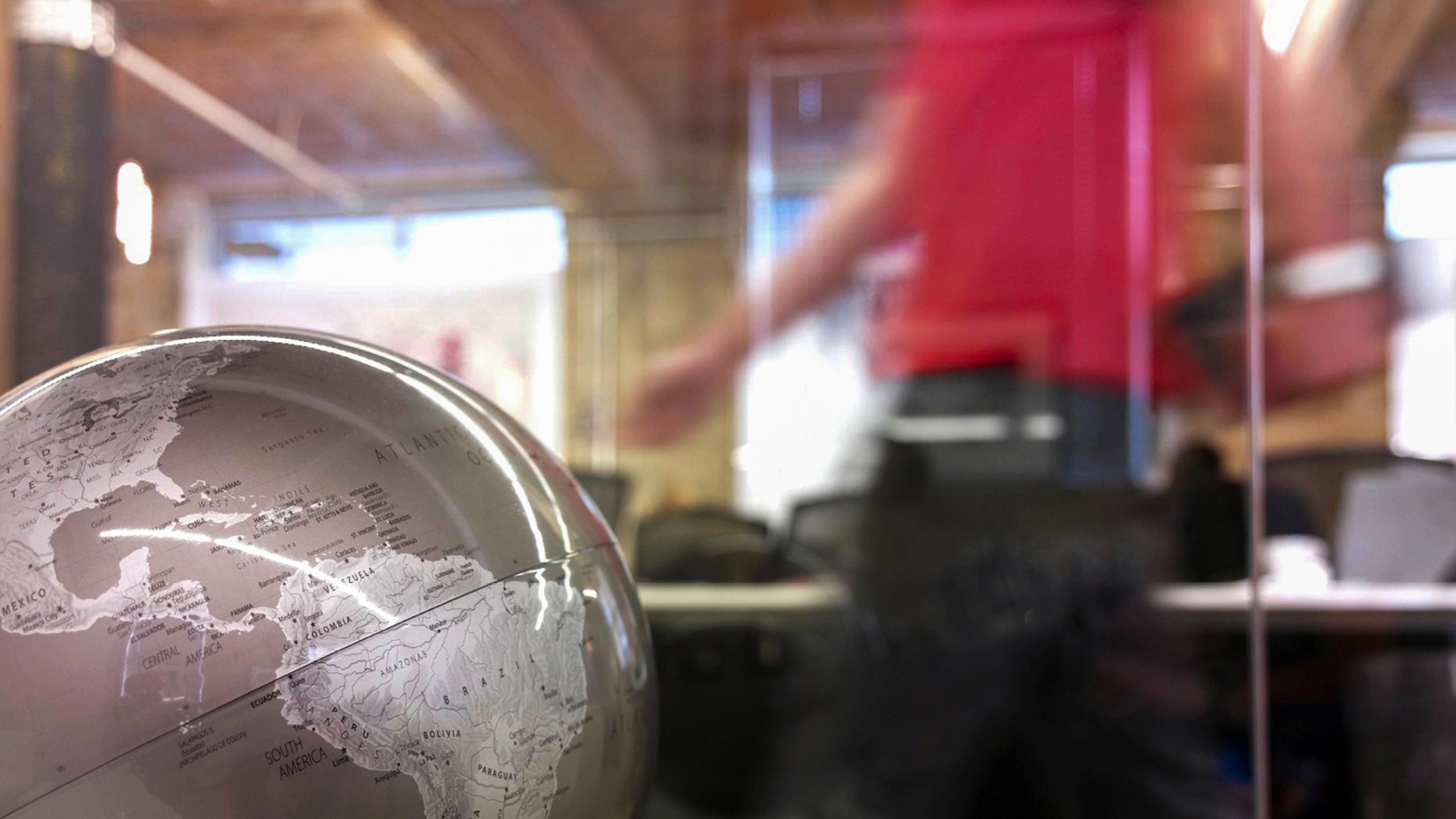 Photo of an office. There is a globe in the foreground. The background is blurred. 