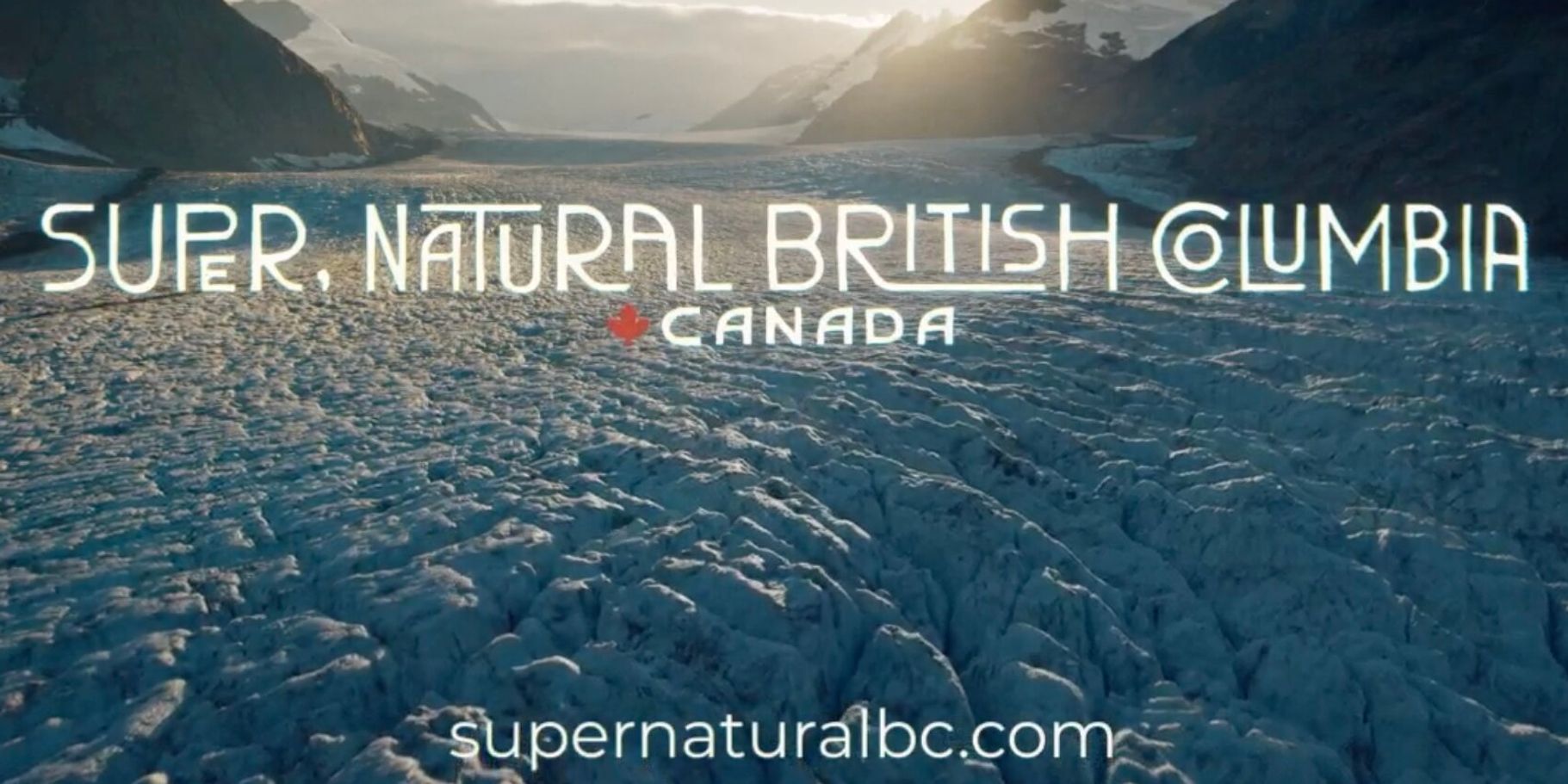 A vast, icy glacier stretches between dark mountain peaks, bathed in golden sunset light. Text reads, “Super, Natural British Columbia, Canada.” Calm and majestic.