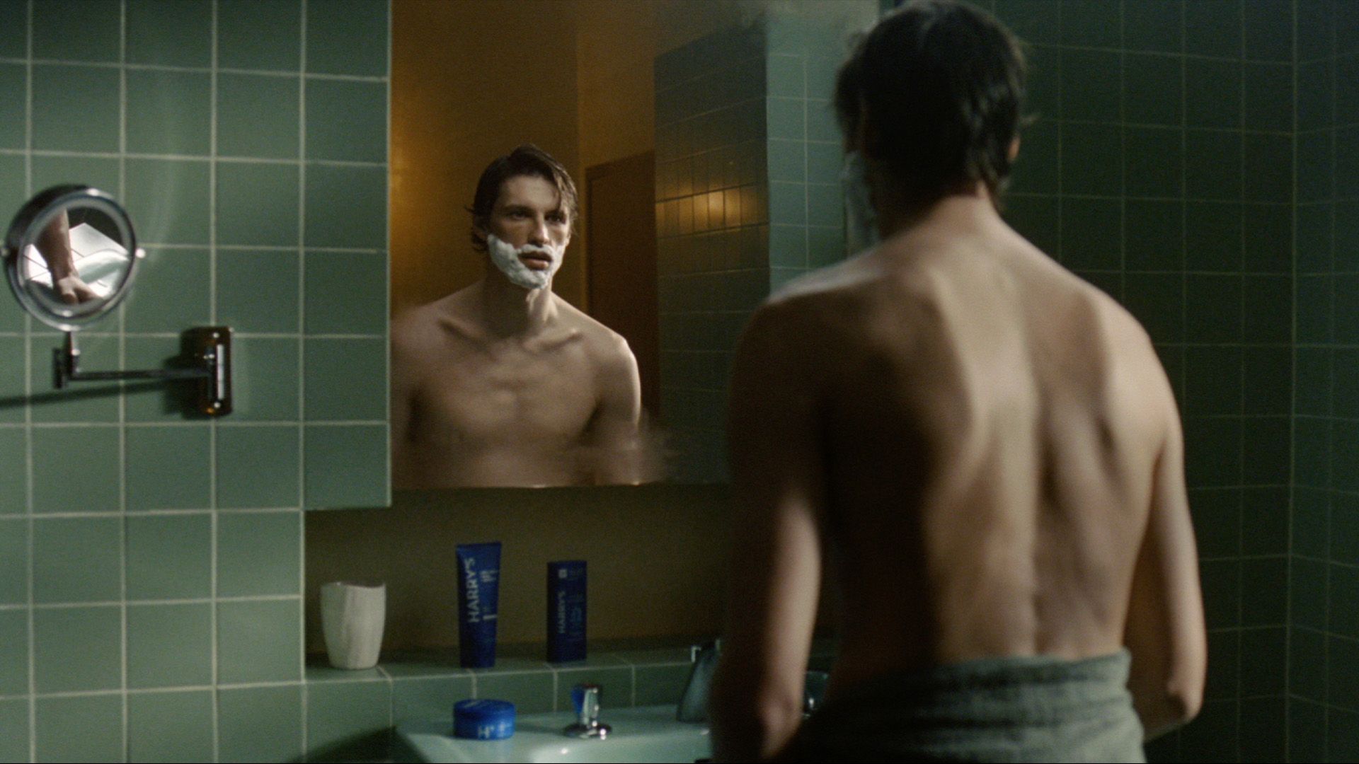 A photo of a man shaving his face in the bathroom mirror.