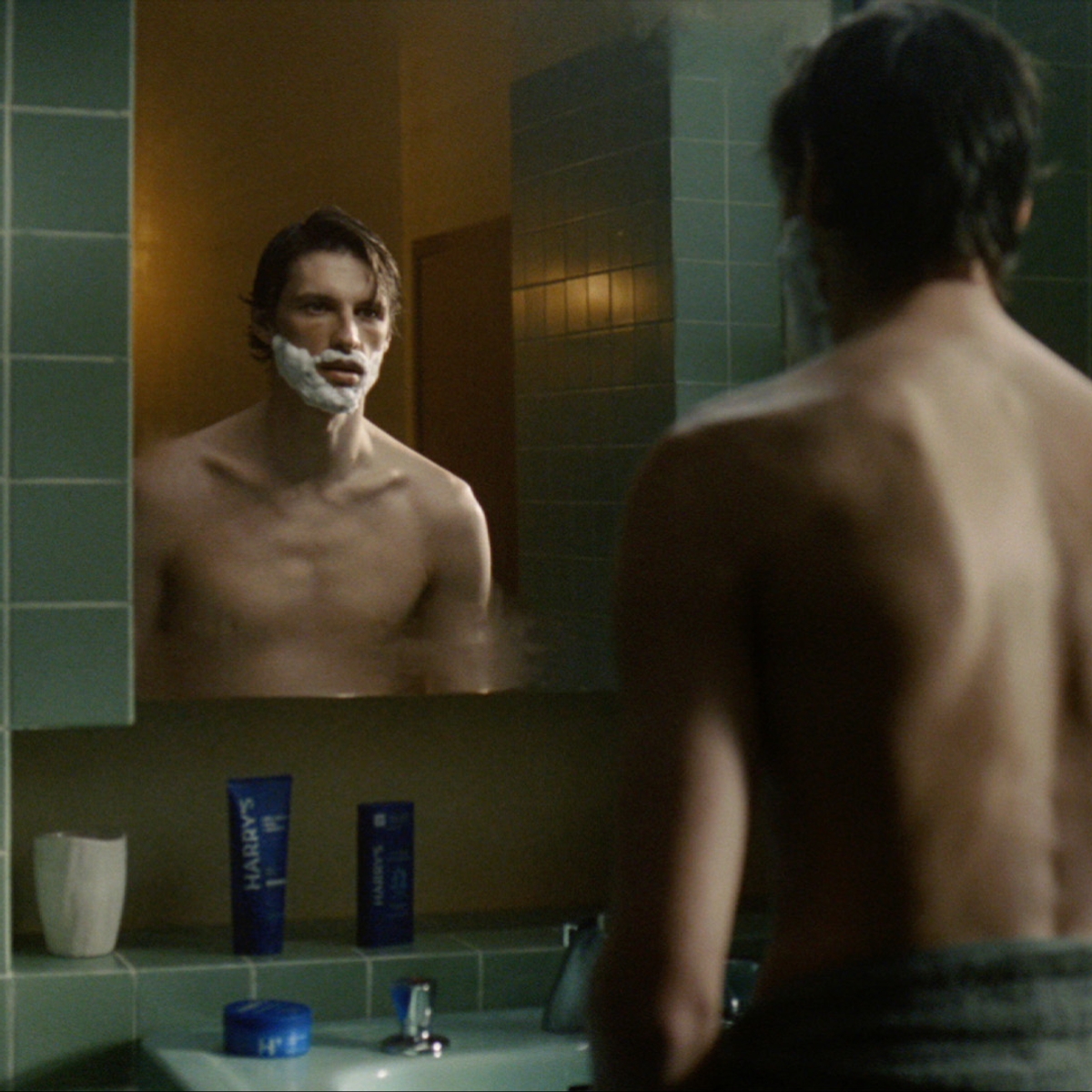 A photo of a man shaving his face in the bathroom mirror.
