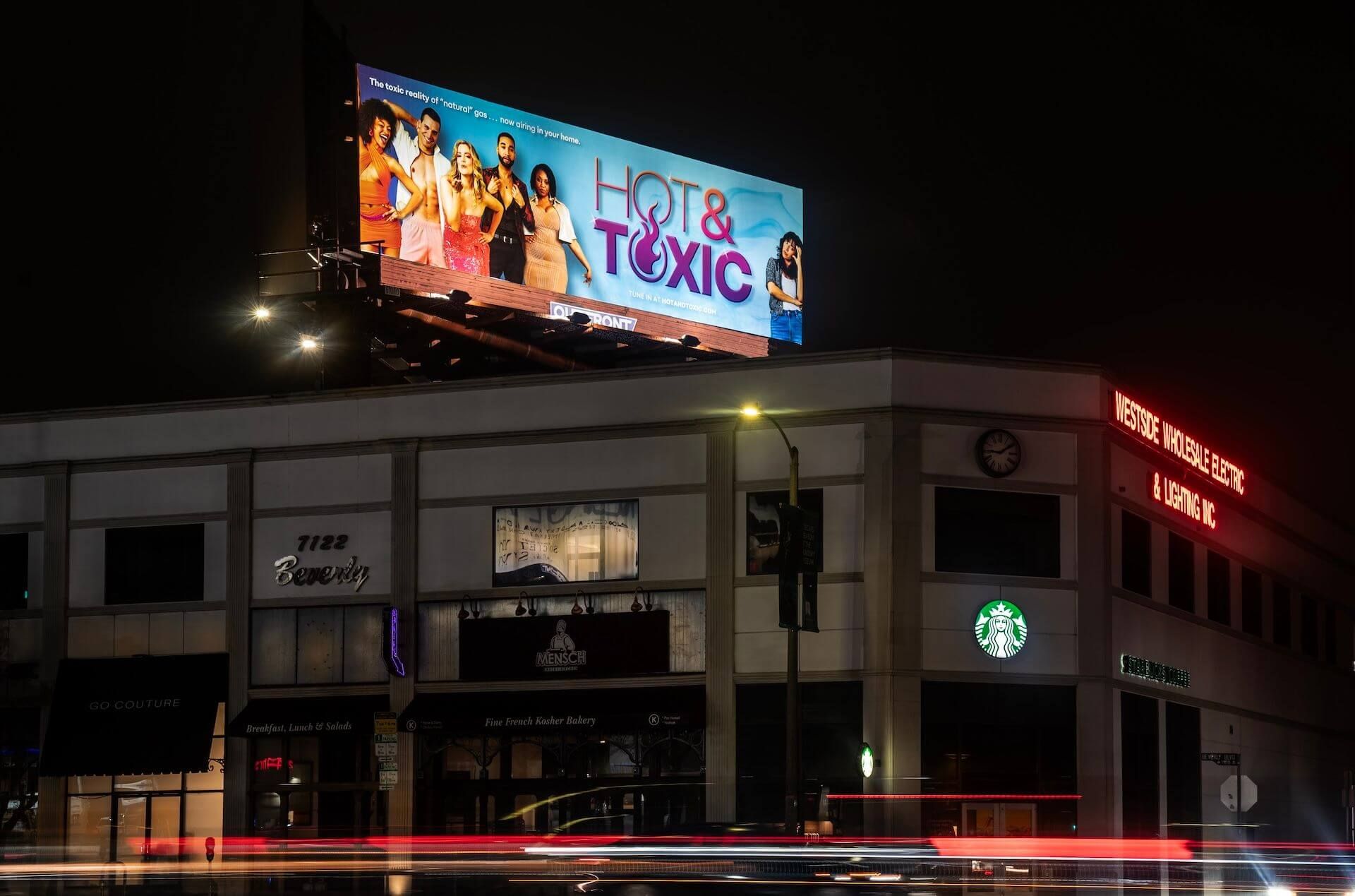 A Hot & Toxic billboard on top of a building in the middle of the night.