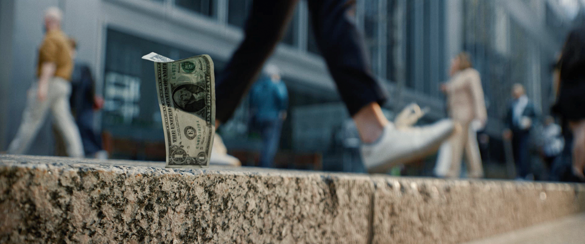 A one-dollar bill stands on a city ledge as blurred pedestrians hurry past, symbolizing money, urban life, opportunity, and financial uncertainty.