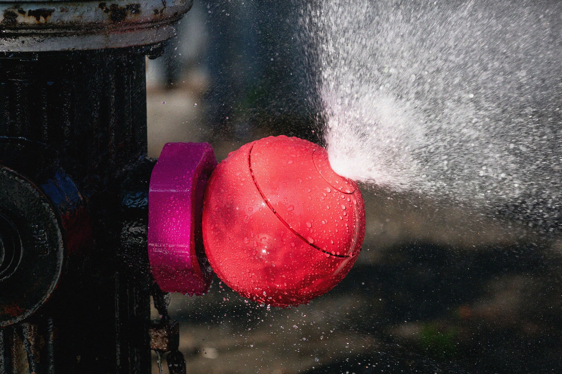 A bright red Splash Spot fire hydrant cap splashing water on the street.