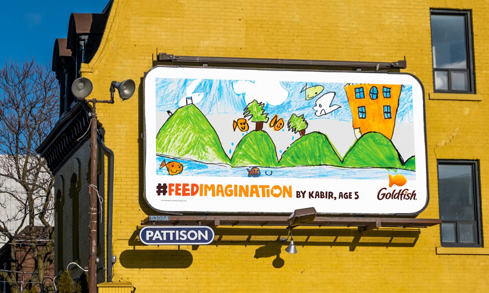 A billboard on the side of a building featuring a child's drawing of goldfish crackers swimming above rolling green hills.