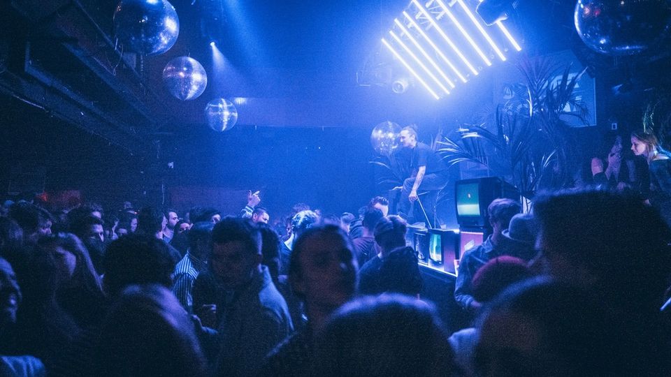 Crowd dancing under atmospheric blue stage lighting at a club show during ADE week