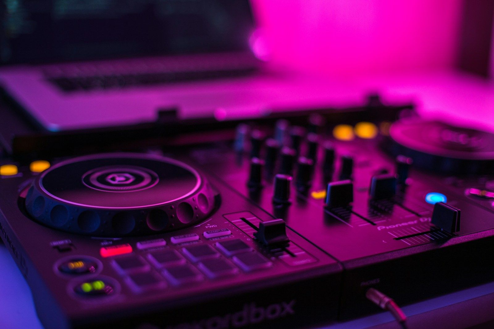 Pioneer DJ mixer pitch faders in a dark studio environment with colourful stage lighting