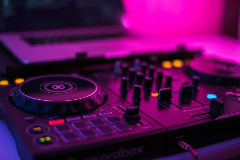 Pioneer DJ mixer pitch faders in a dark studio environment with colourful stage lighting