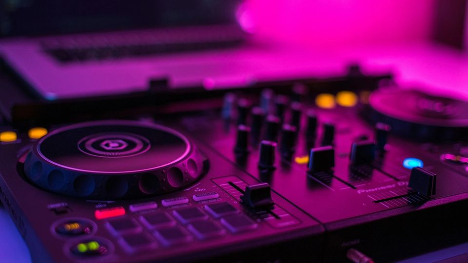 Pioneer DJ mixer pitch faders in a dark studio environment with colourful stage lighting