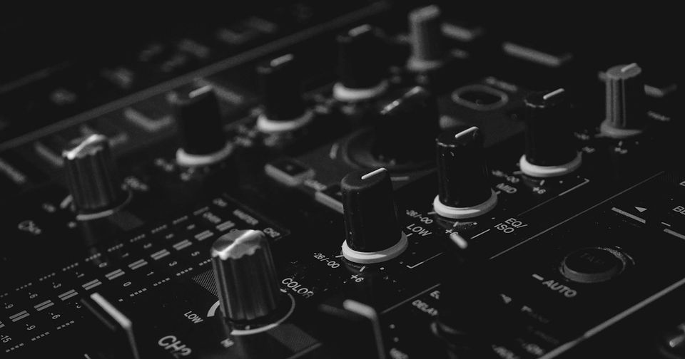 Close-up of a professional DJ mixer showing EQ knobs, channel faders, and controls