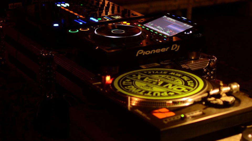 A DJ performing in atmospheric dark lighting at an intimate venue