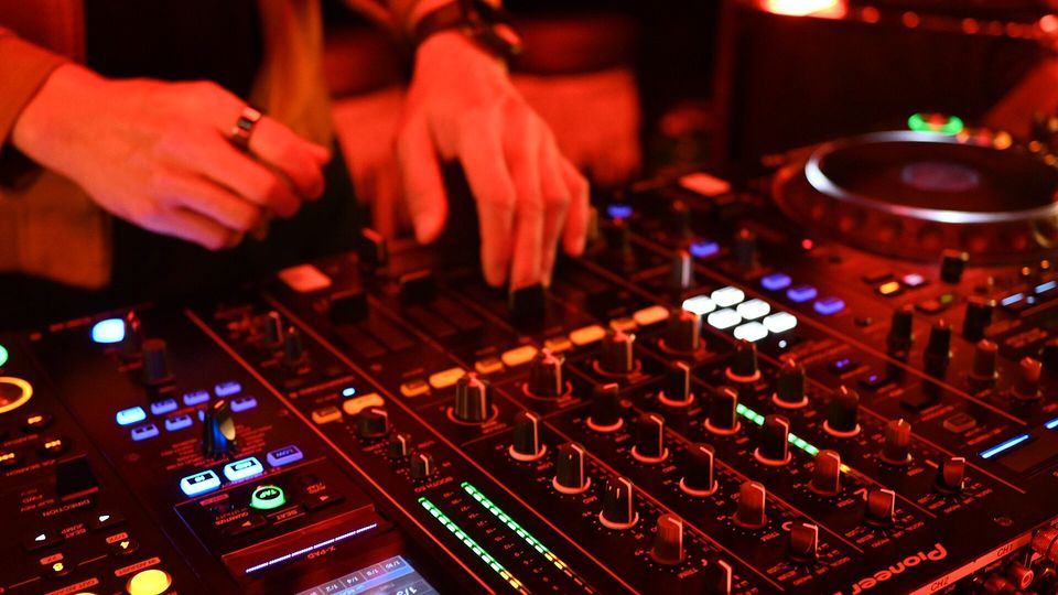 DJ's hands on the channel faders of a Pioneer DJ mixer under red club lights