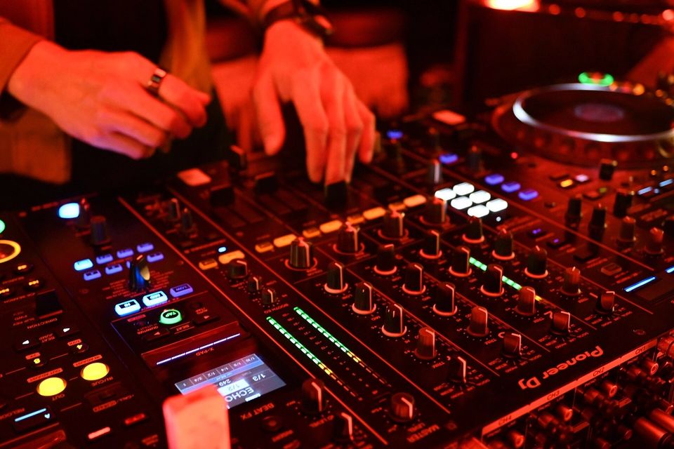 DJ's hands on the channel faders of a Pioneer DJ mixer under red club lights