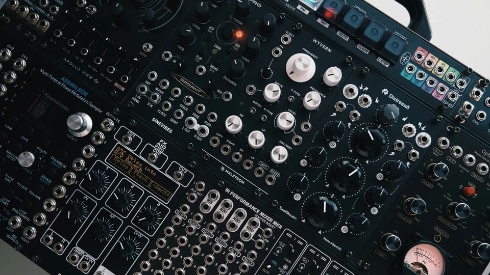 Close-up of a modular synthesizer panel with patch cables and knobs in dark studio light