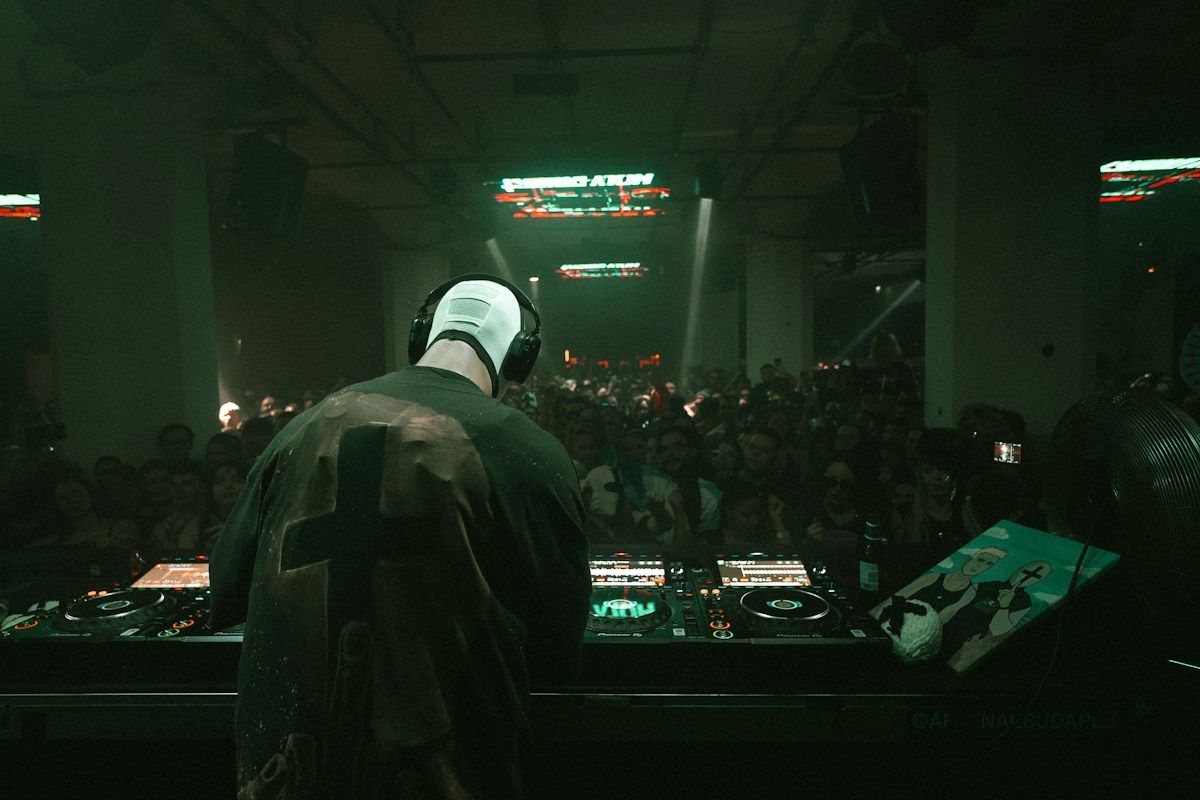 DJ silhouetted from behind at Pioneer booth facing large warehouse crowd