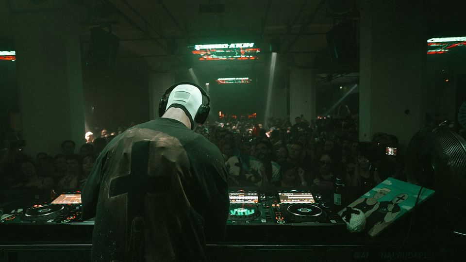 DJ silhouetted from behind at Pioneer booth facing large warehouse crowd